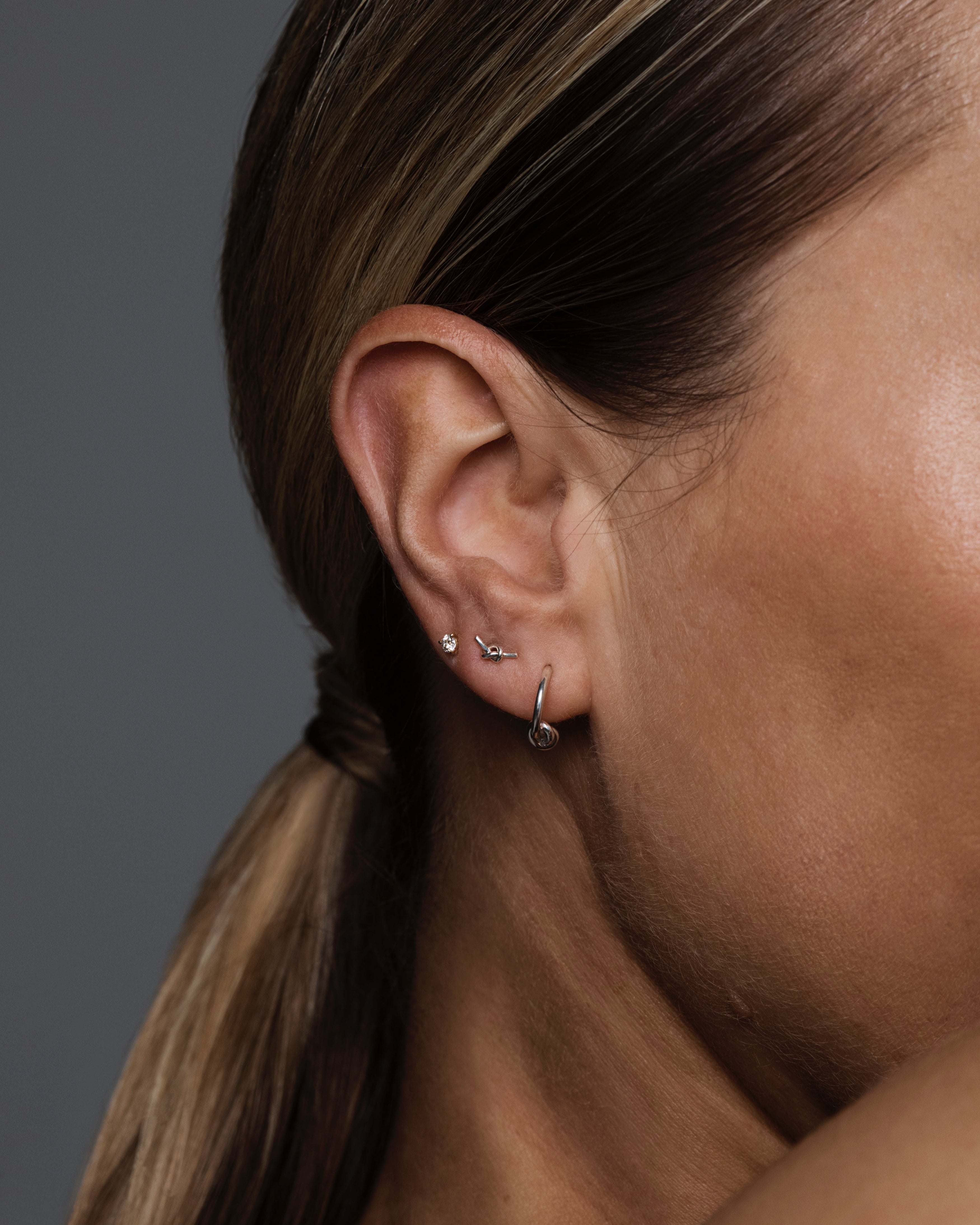 A close up on an ear stacked with the Cara Studs, Da Anam Hoops and a diamond stud.