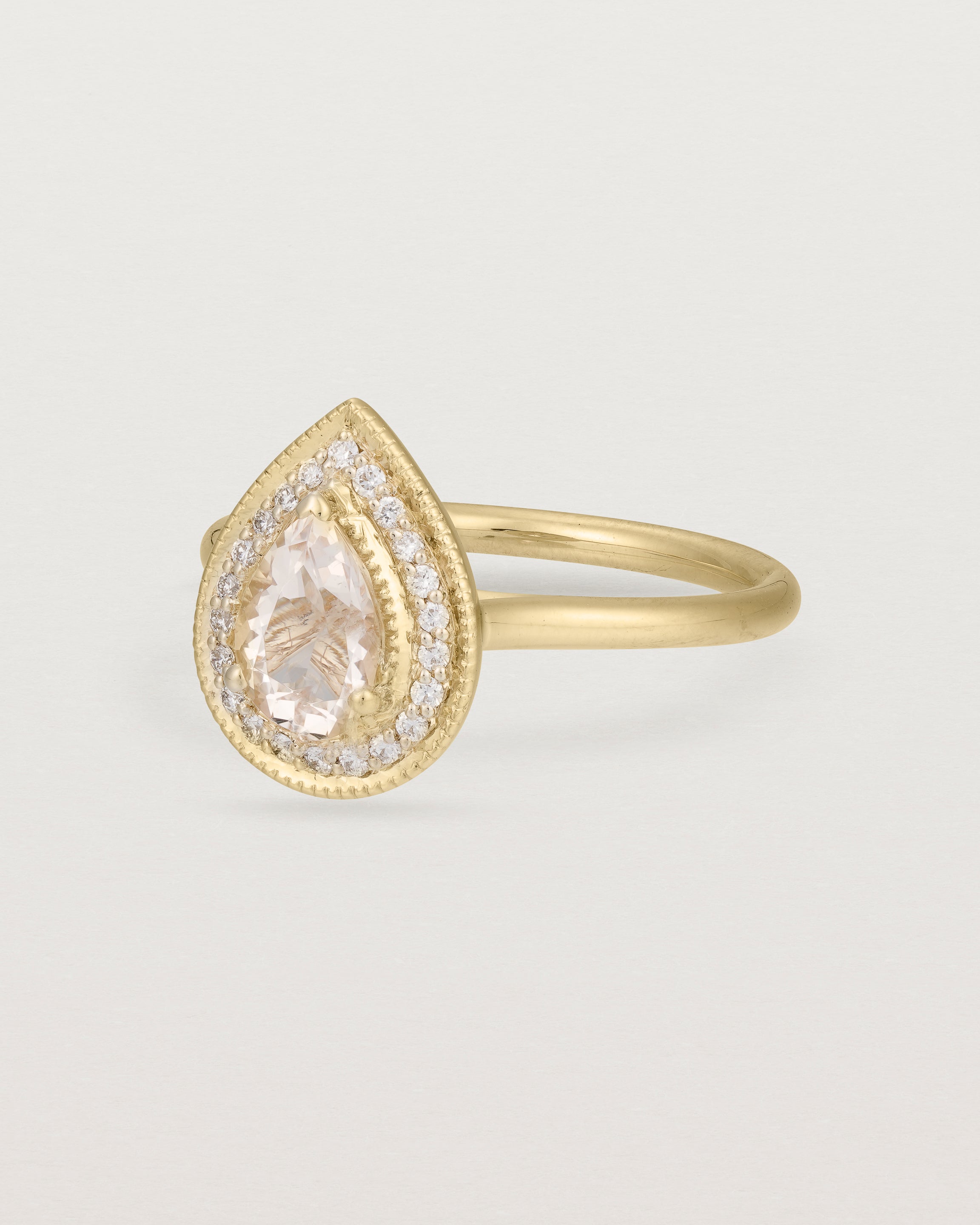 Side view pear halo ring featuring a pear cut pale pink morganite and a halo of white diamonds in yellow gold