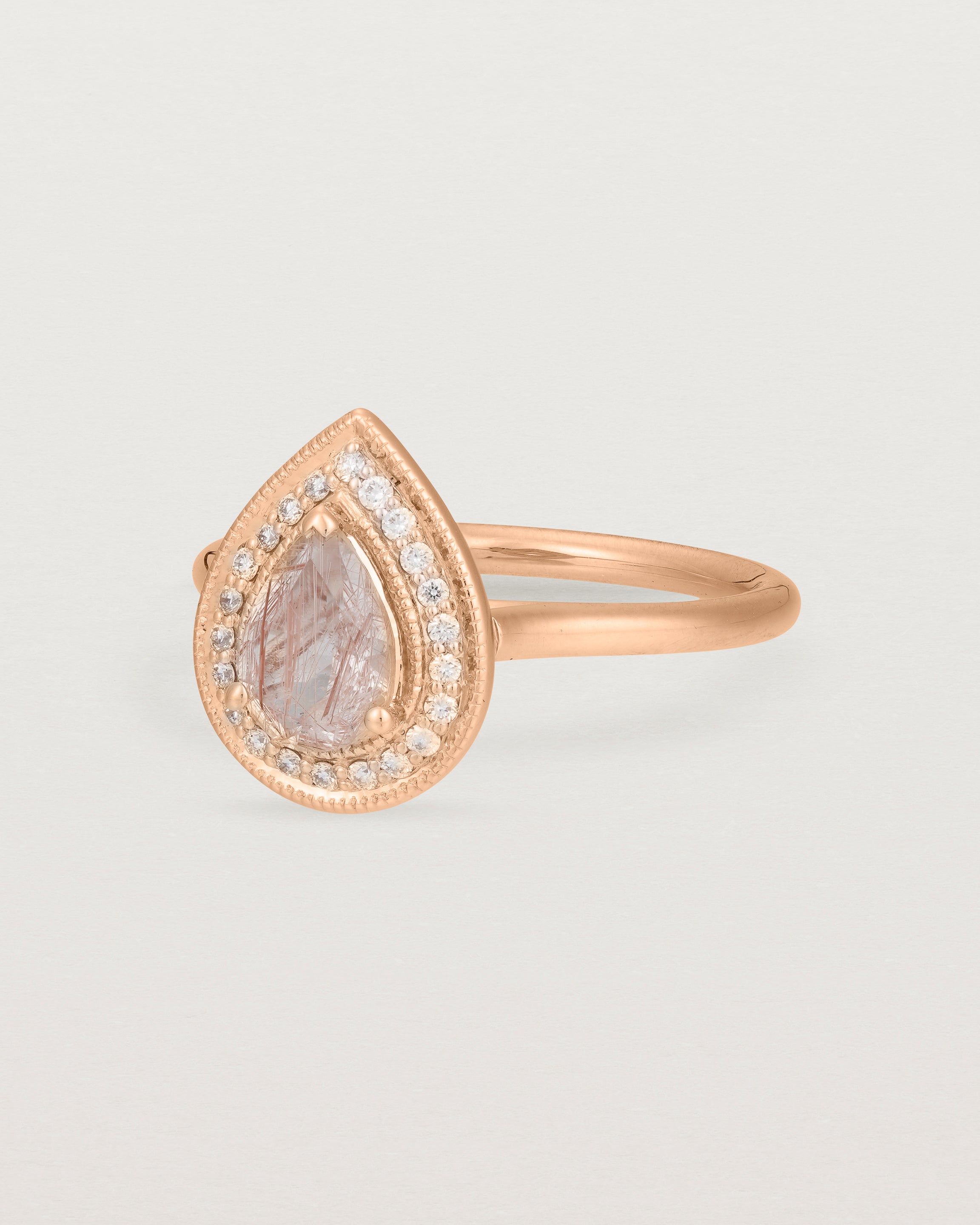Side view pear halo ring featuring a pear cut rutilated quartz stone and a halo of white diamonds in rose gold