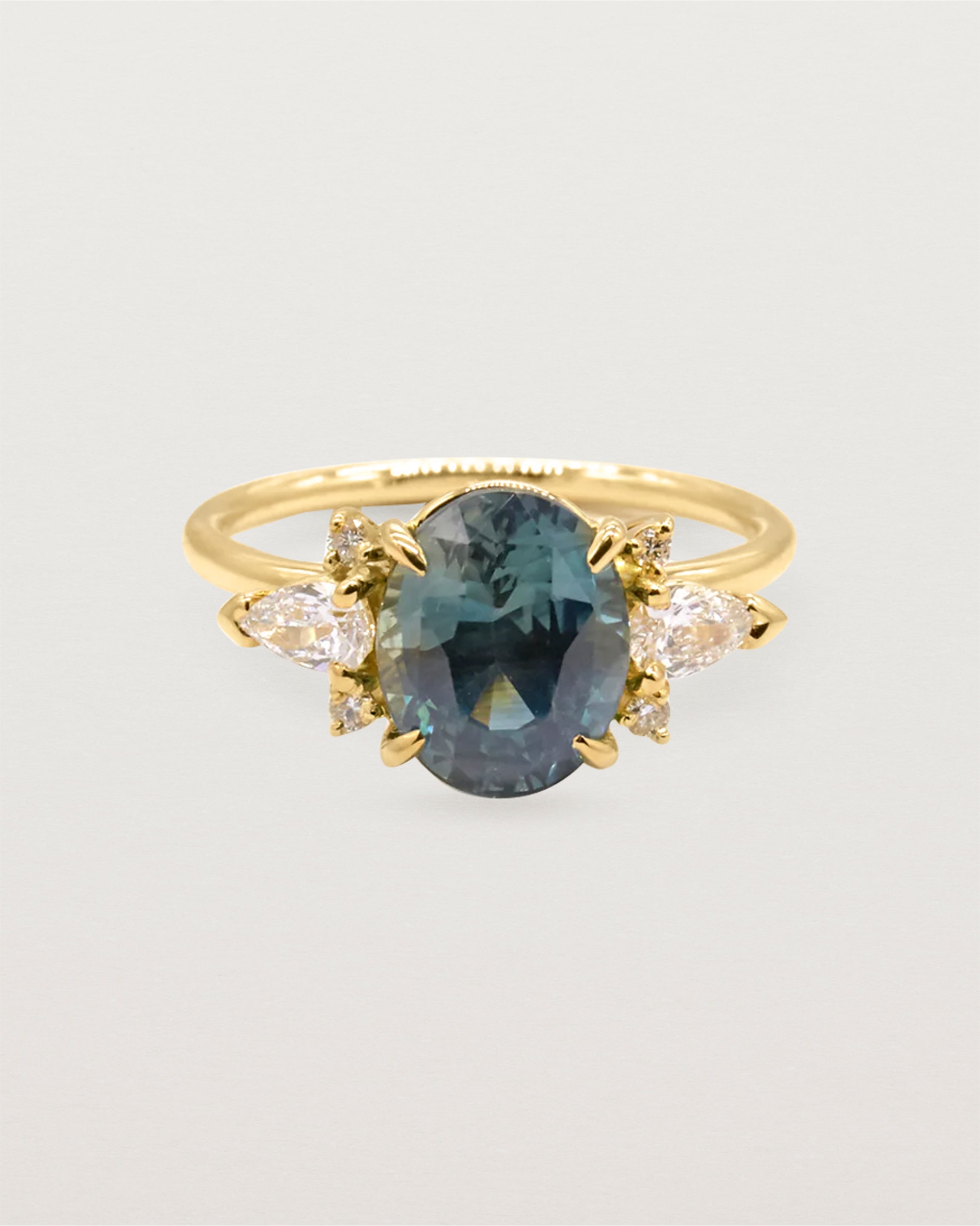 A large oval teal sapphire adorned with white diamond clusters, crafted in yellow gold