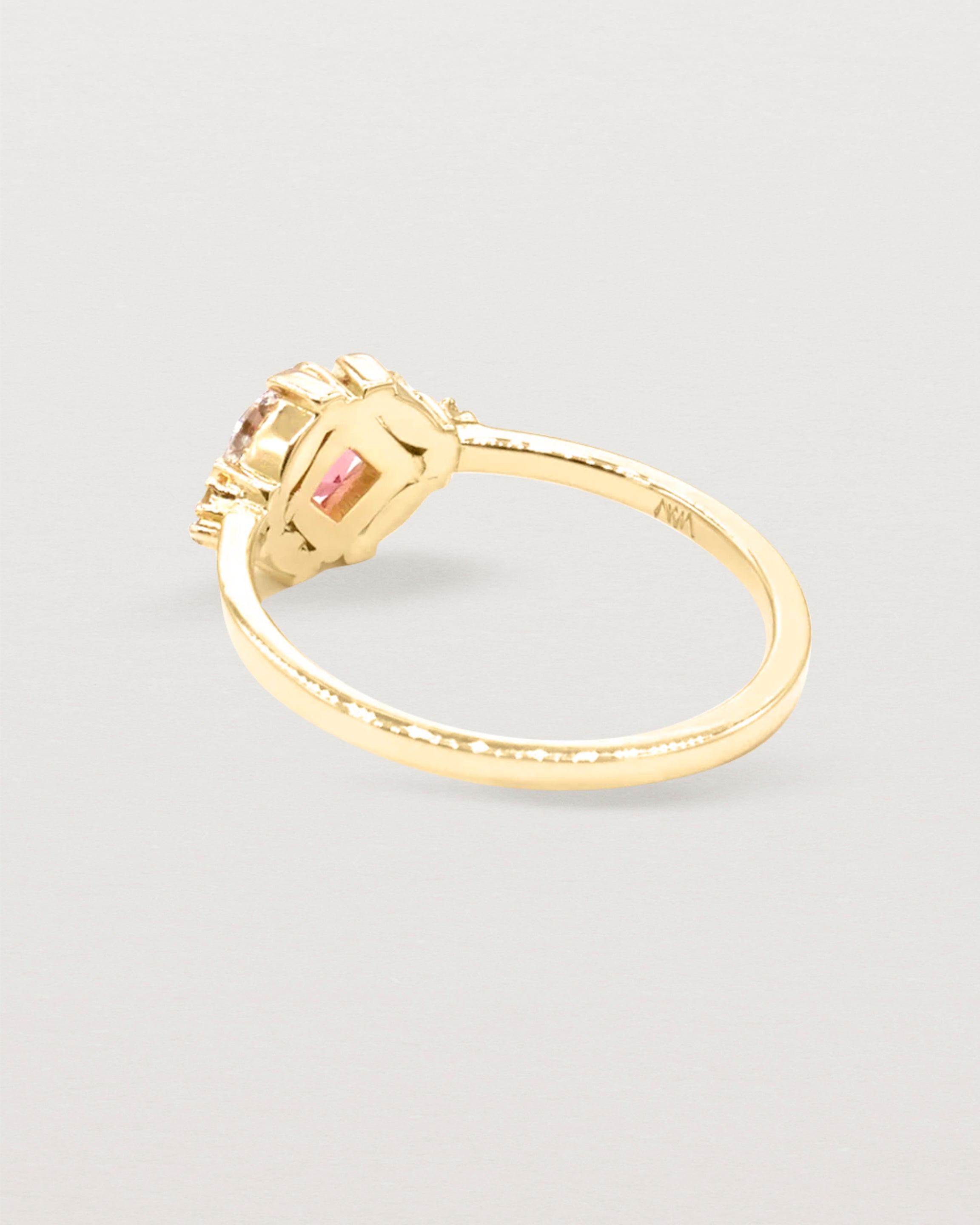 The back view of an asscher cut pink spinel is heroes by white diamond clusters set in yellow gold.