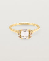 A emerald cut white diamond is shouldered by sparkling champagne diamonds and crafted in yellow gold. 