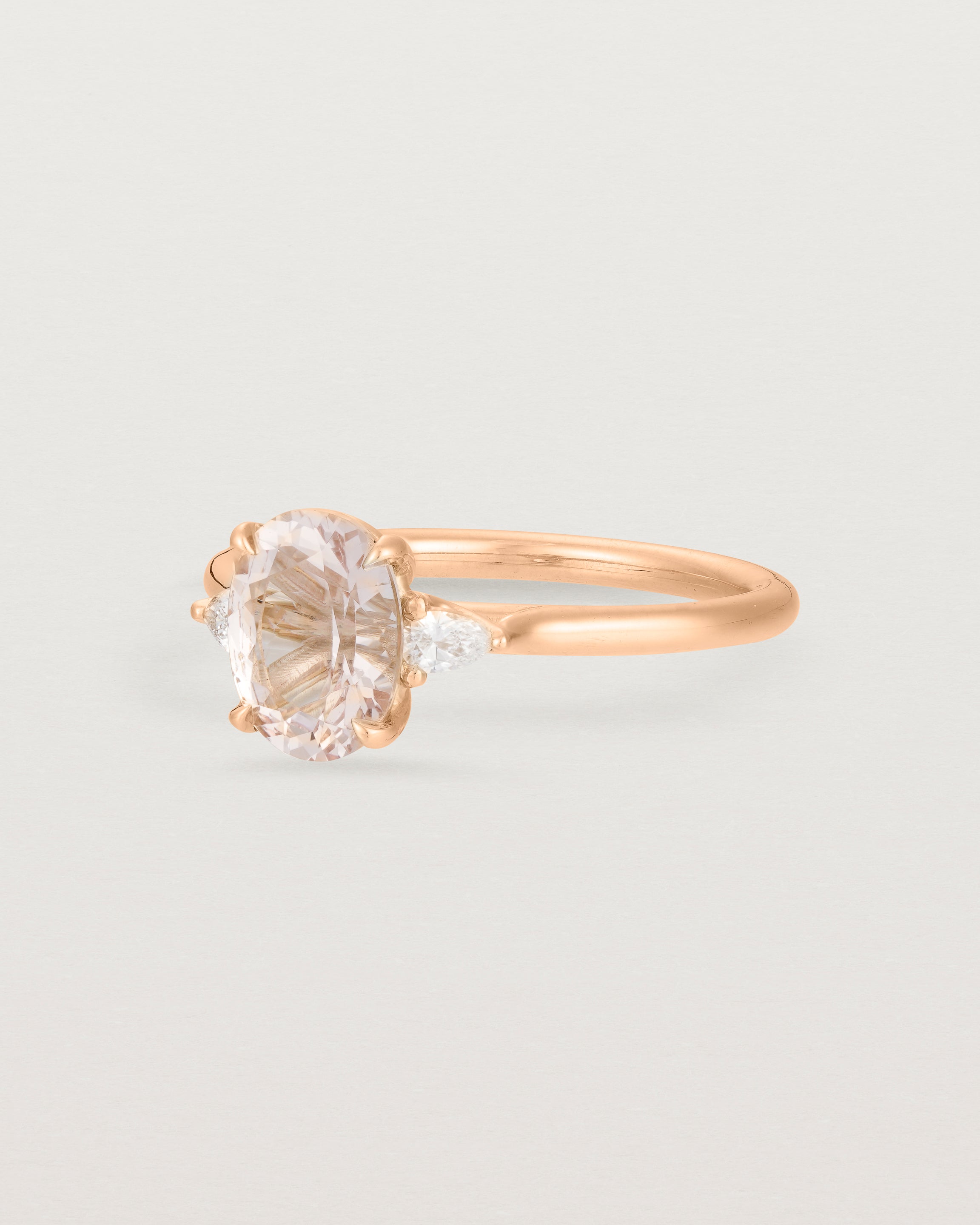 Side view of an Oval morganite adorned with white diamonds on either side, featuring a sweeping setting and crafted in rose gold