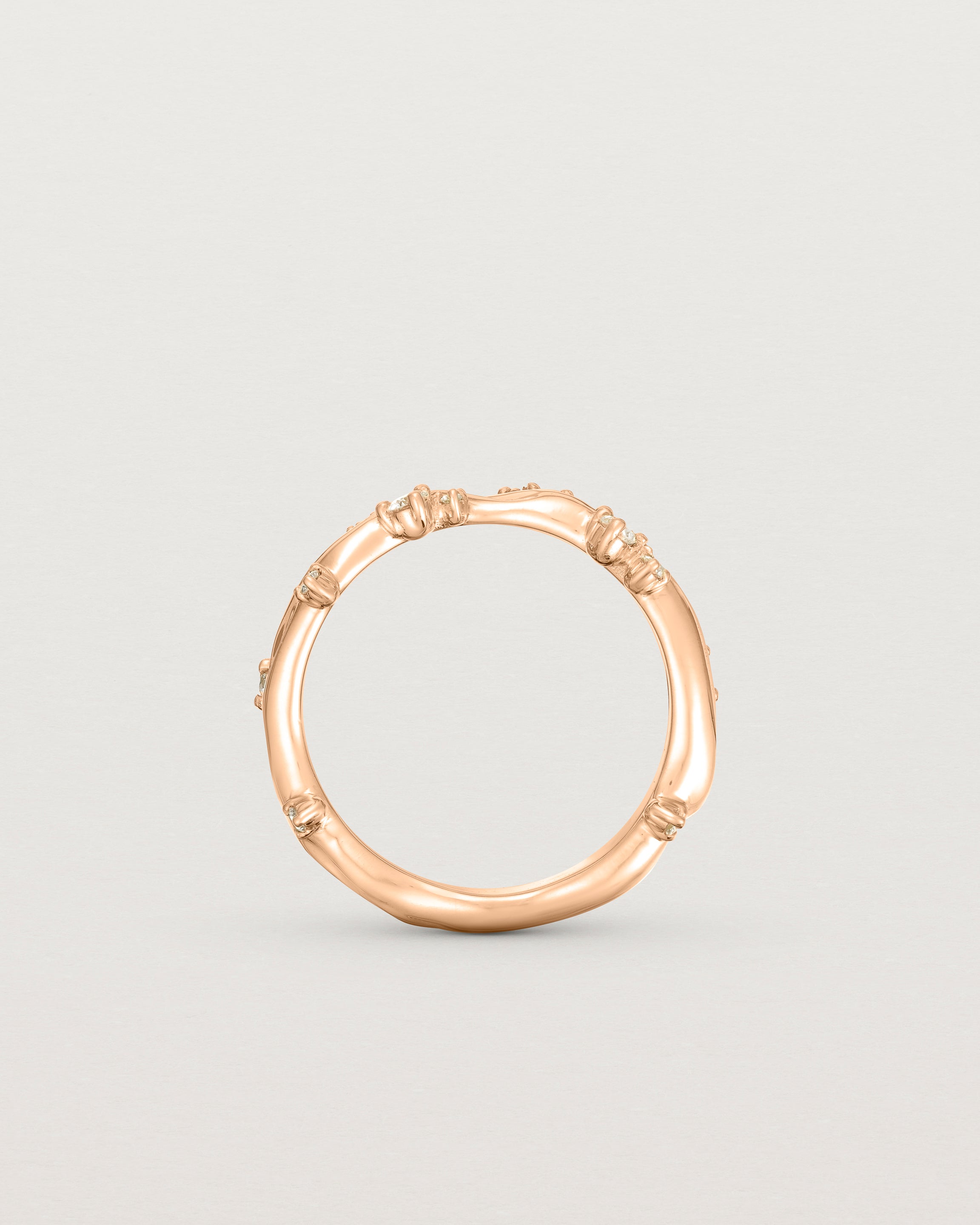 Product photo of the rose gold Ember ring with white diamonds scattered around the band standing up.