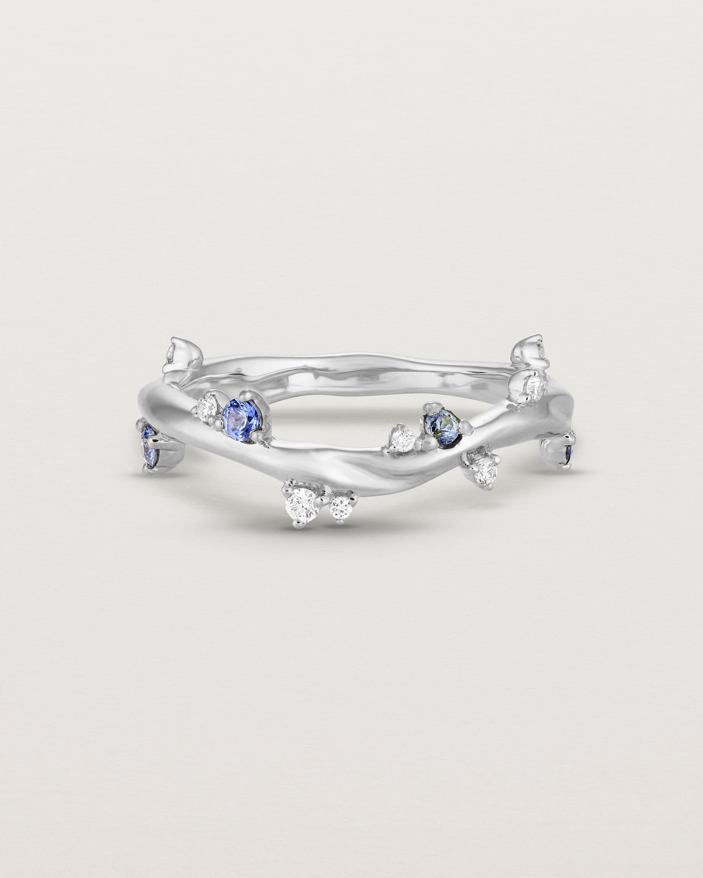 Front image of the Ember ring in white gold featuring a scattering of white diamonds and blue sapphires.