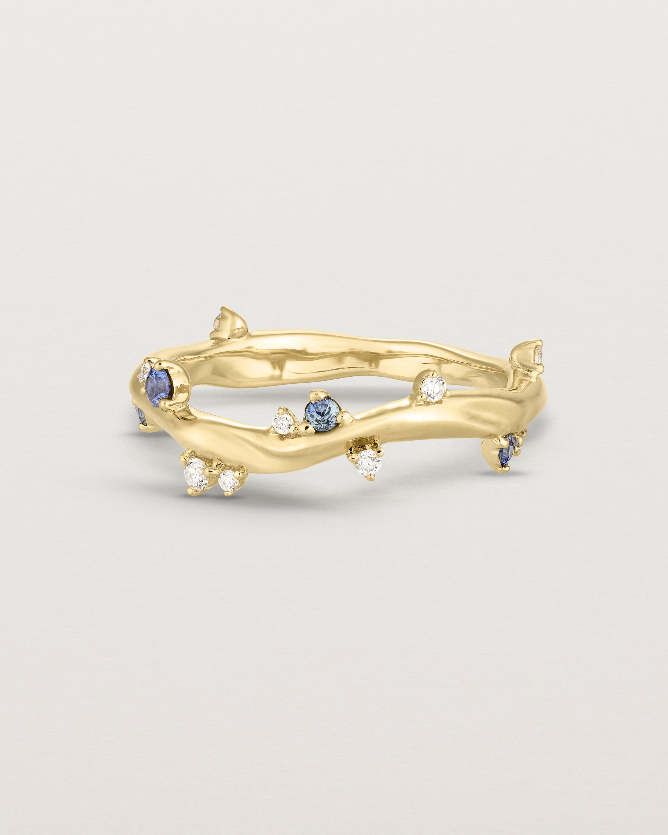 Front image of the Ember ring in yellow gold featuring a scattering of white diamonds and blue sapphires.
