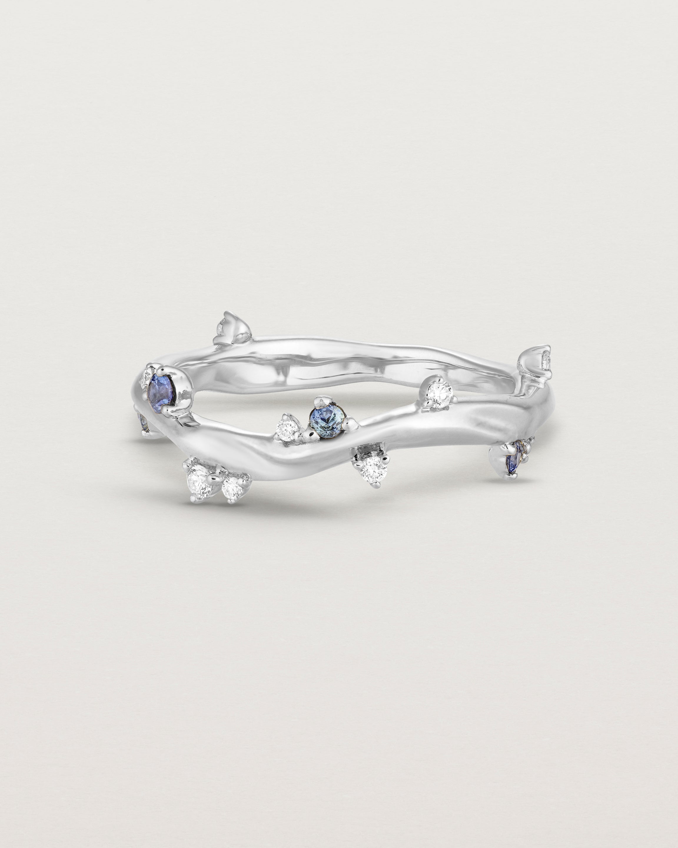 Front image of the Ember ring in white gold featuring a scattering of white diamonds and blue sapphires.