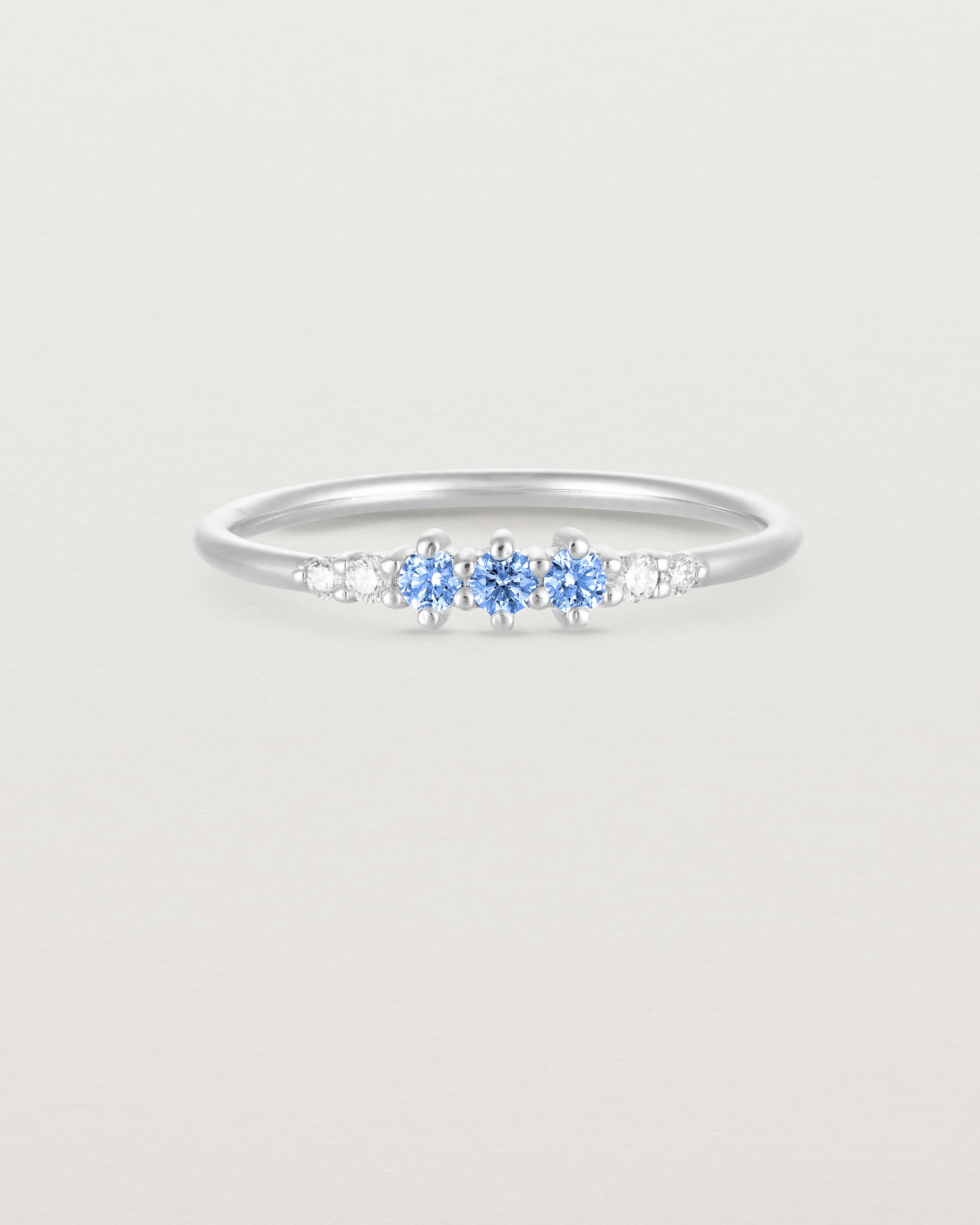 Front facing deep etched image of a white gold ring with blue topaz birthstones and diamonds.