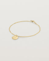 A yellow gold chain bracelet featuring a disc with an engraved letter m