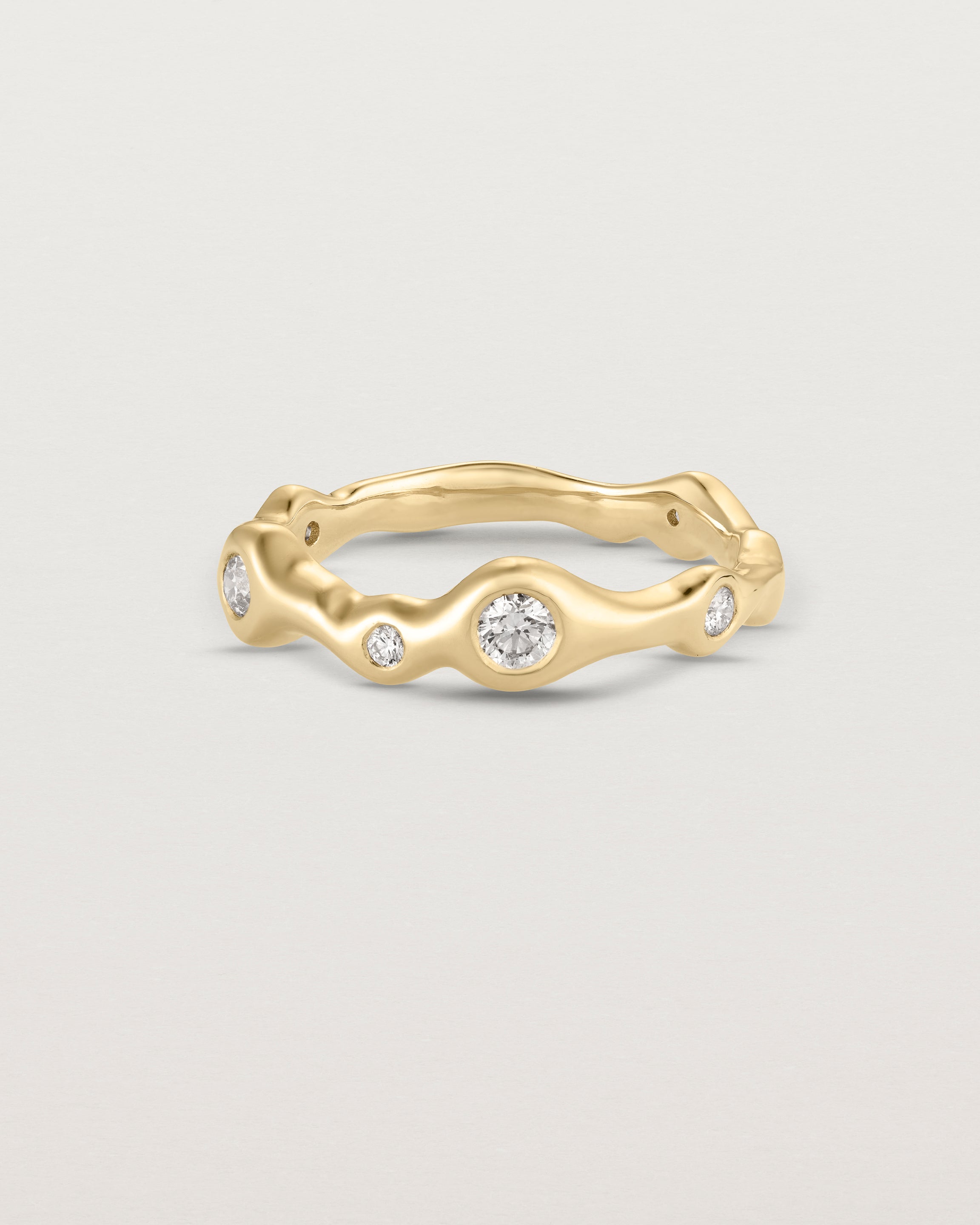 Front on deep etched image of a yellow gold ring with seven scattered white diamonds.
