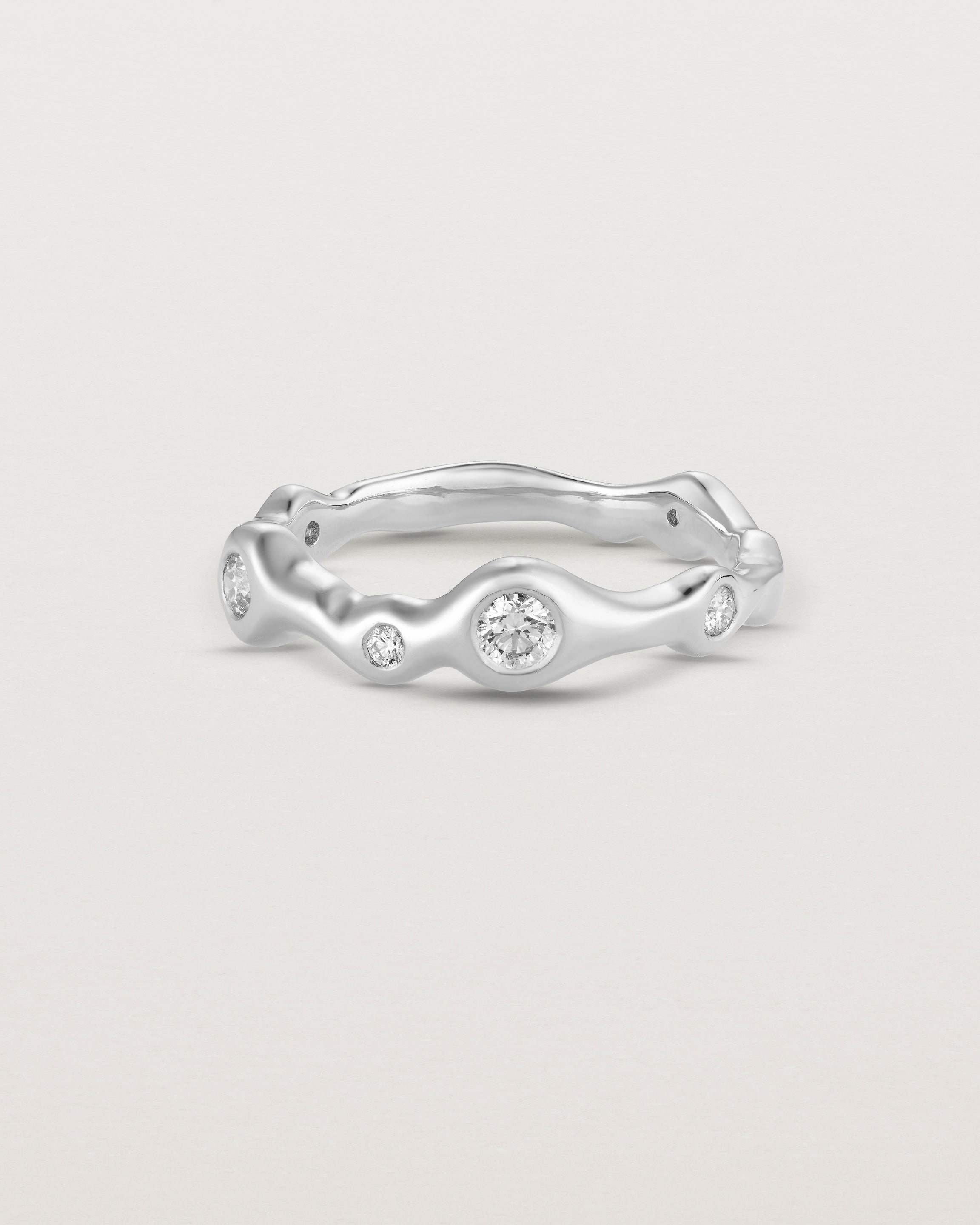 Front on deep etched image of a white gold ring with seven scattered white diamonds.