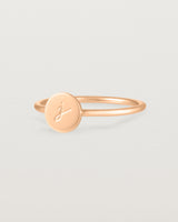 Angled view of a rose gold ring featuring a disc with the letter j engraved