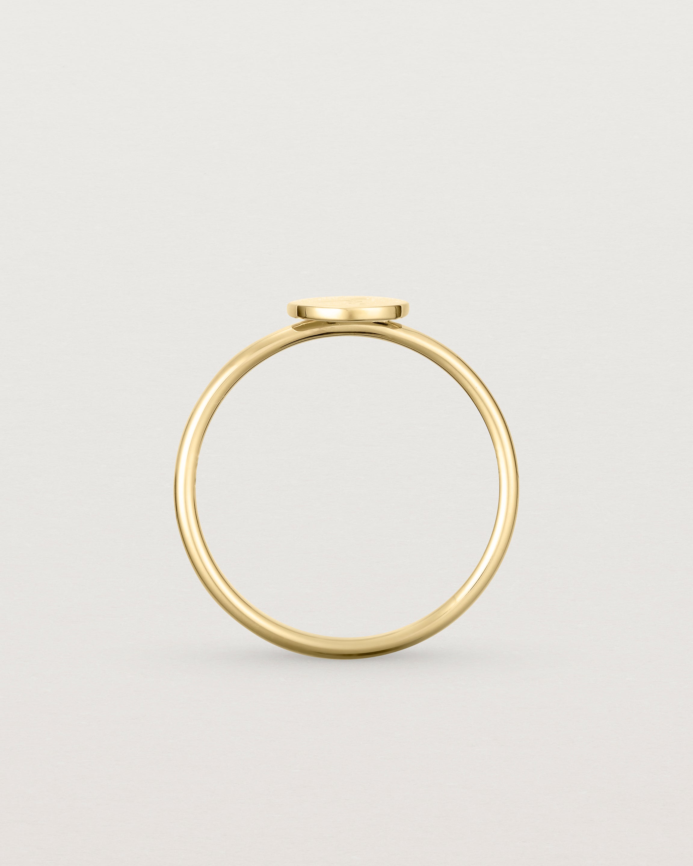 Standing view of a yellow gold ring featuring a disc with the letter j engraved