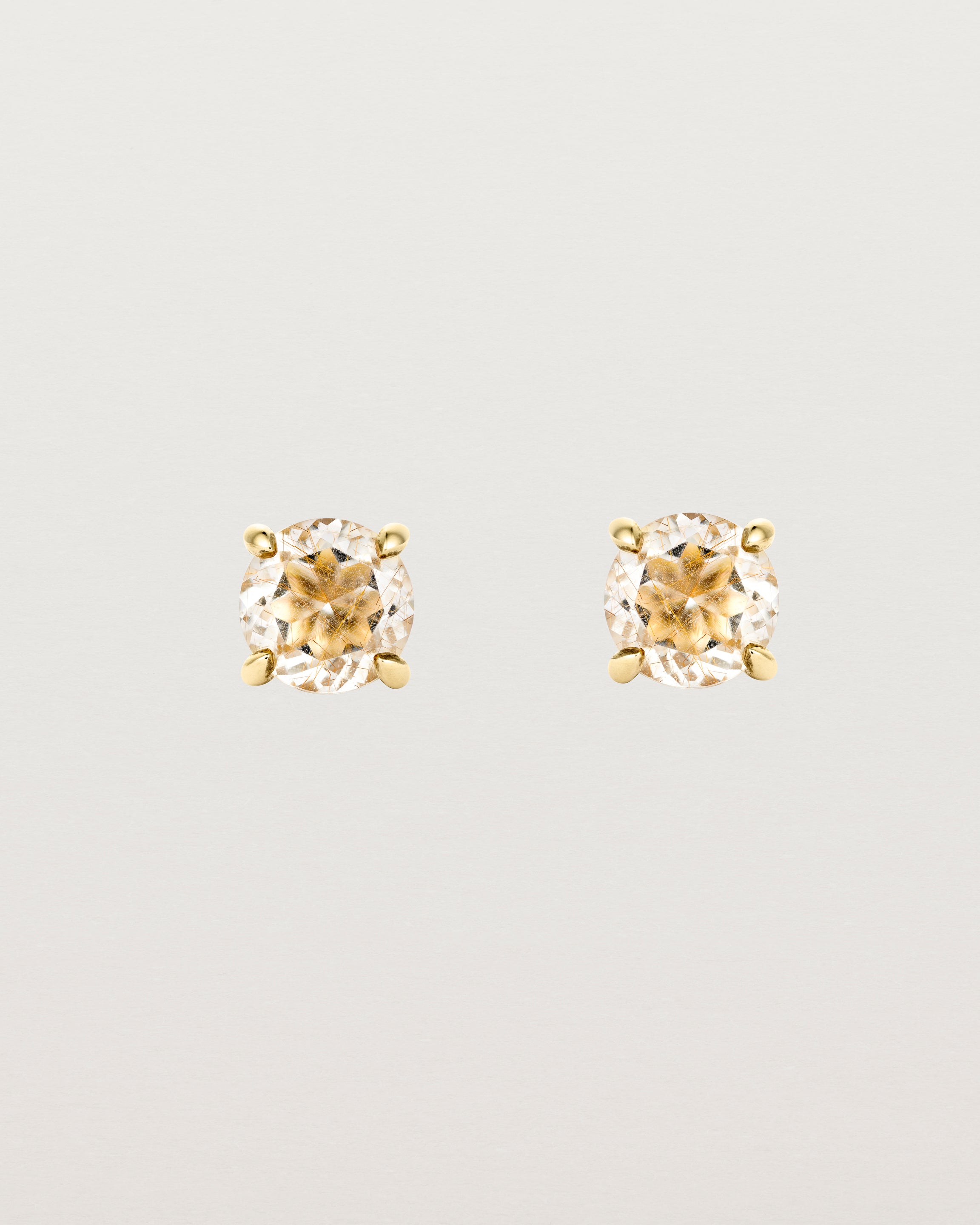 A pair of yellow gold studs featuring a round cut light yellow rutilated quartz stone
