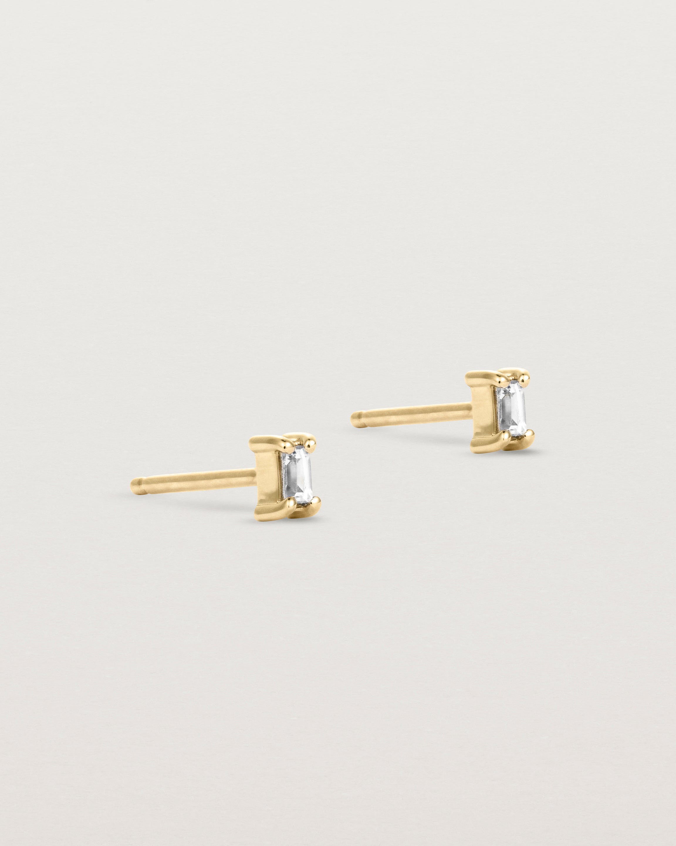 A pair of yellow gold studs featuring an emerald cut white diamond