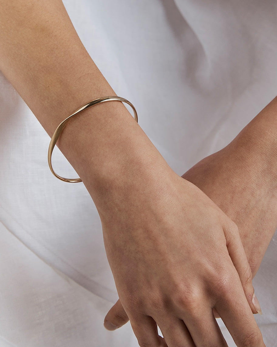 A woman wearing the Ellipse / Shift Bangle in yellow gold.