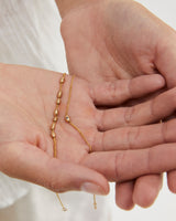 A hand showing the Sonder Bracelet | Birthstone with 1 charm versus 7 charms, both in yellow gold.