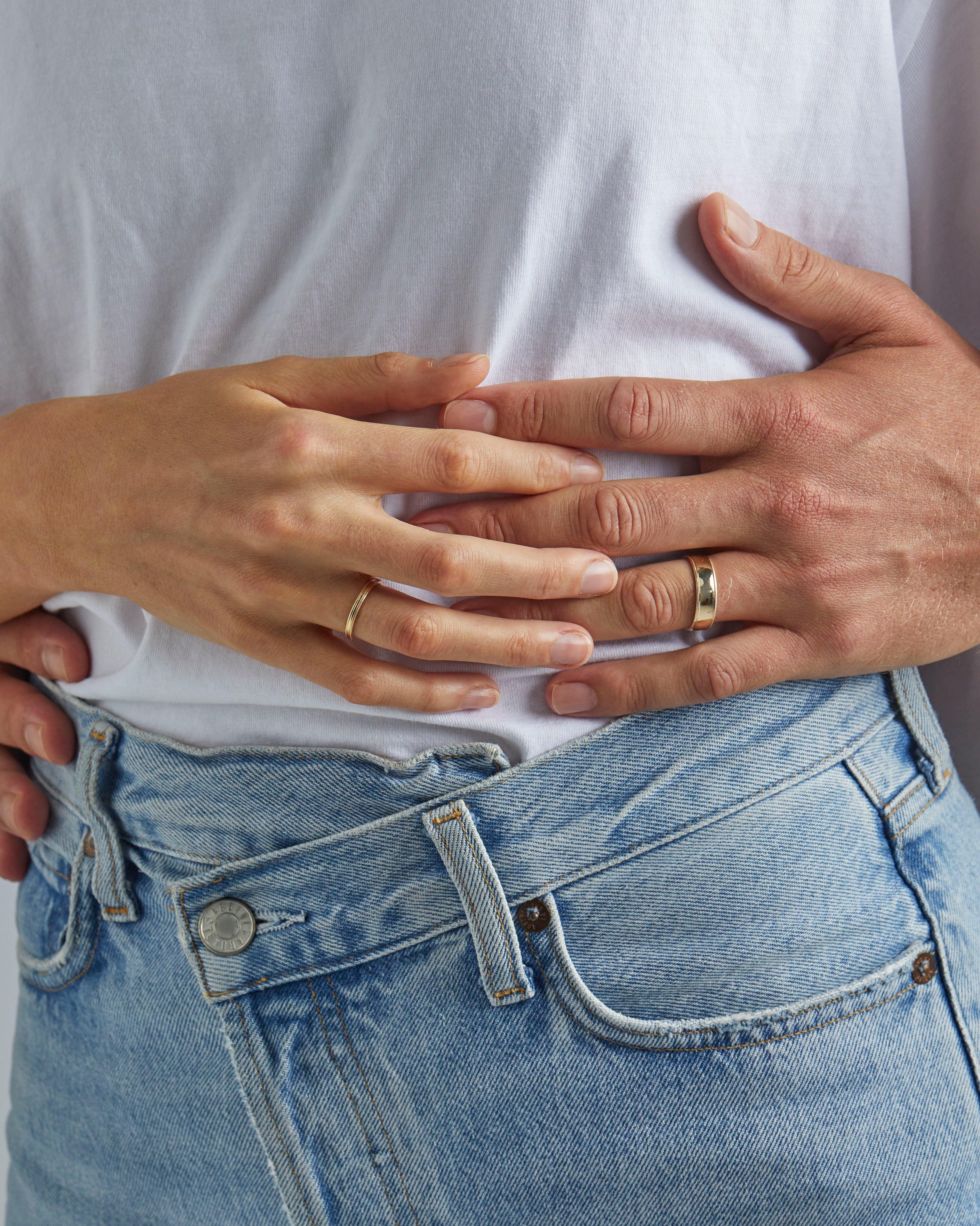 A female wears the 2mm millgrain wedding ring and male model wears the 6mm millgrain wedding ring, in yellow gold