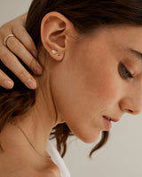 A woman wearing a selection of yellow gold jewellery, including the Tiny Dot Studs in yellow gold.