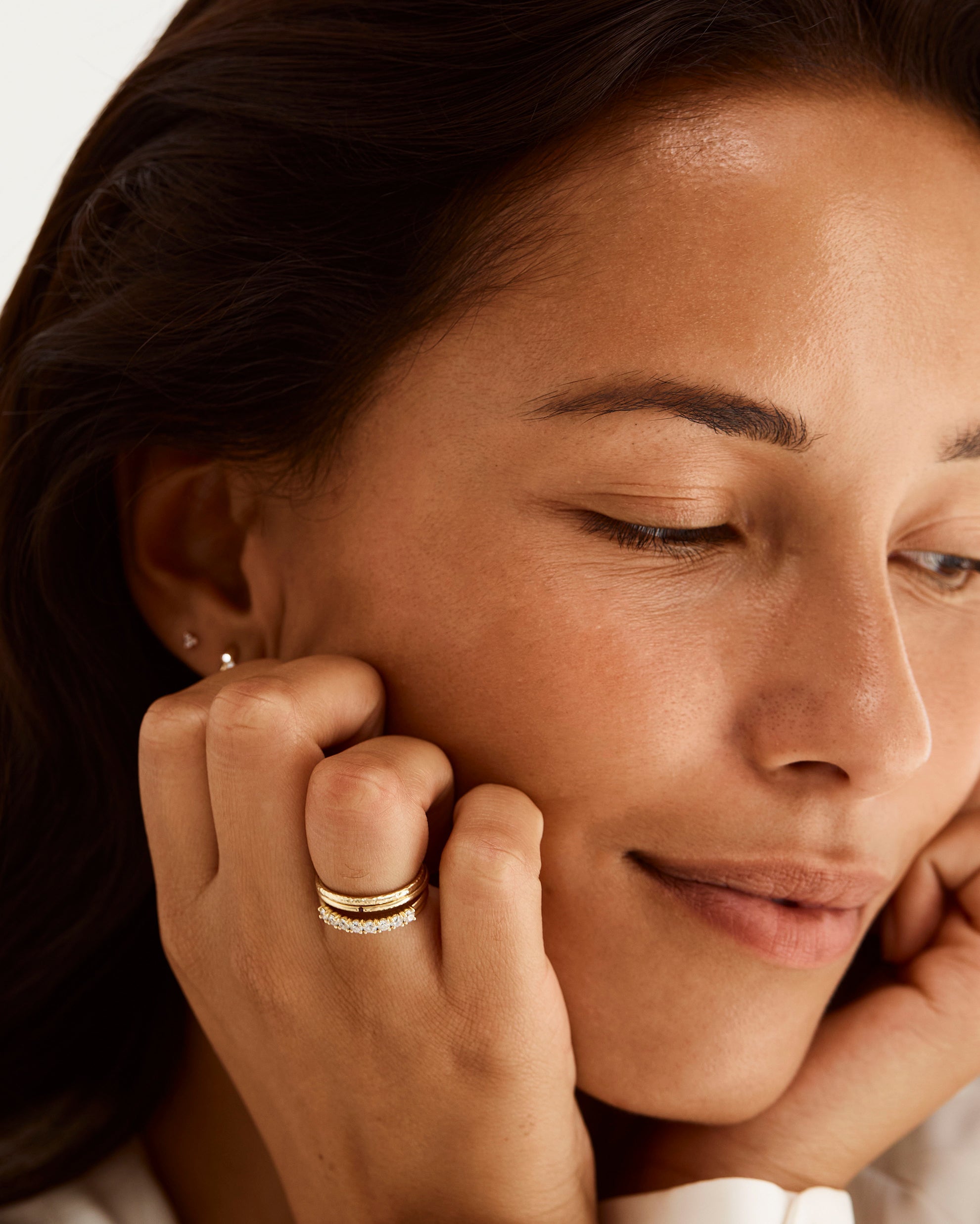 Model wears a round diamond wrap ring, stacked with textured gold bands, including our promise ring with a small sapphire set in the centre. 