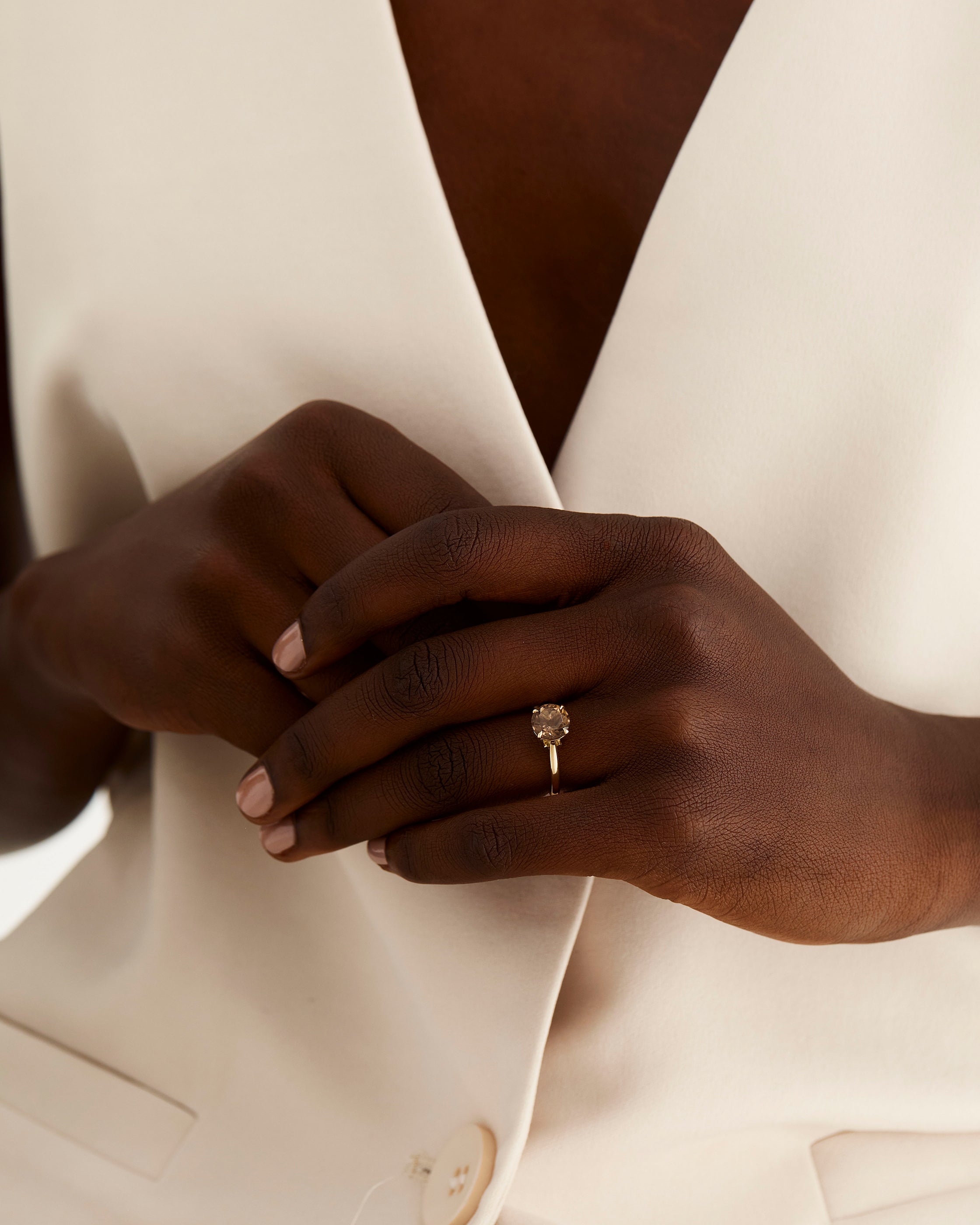 A model wears a round solitaire with a smokey quartz and diamond details in the setting
