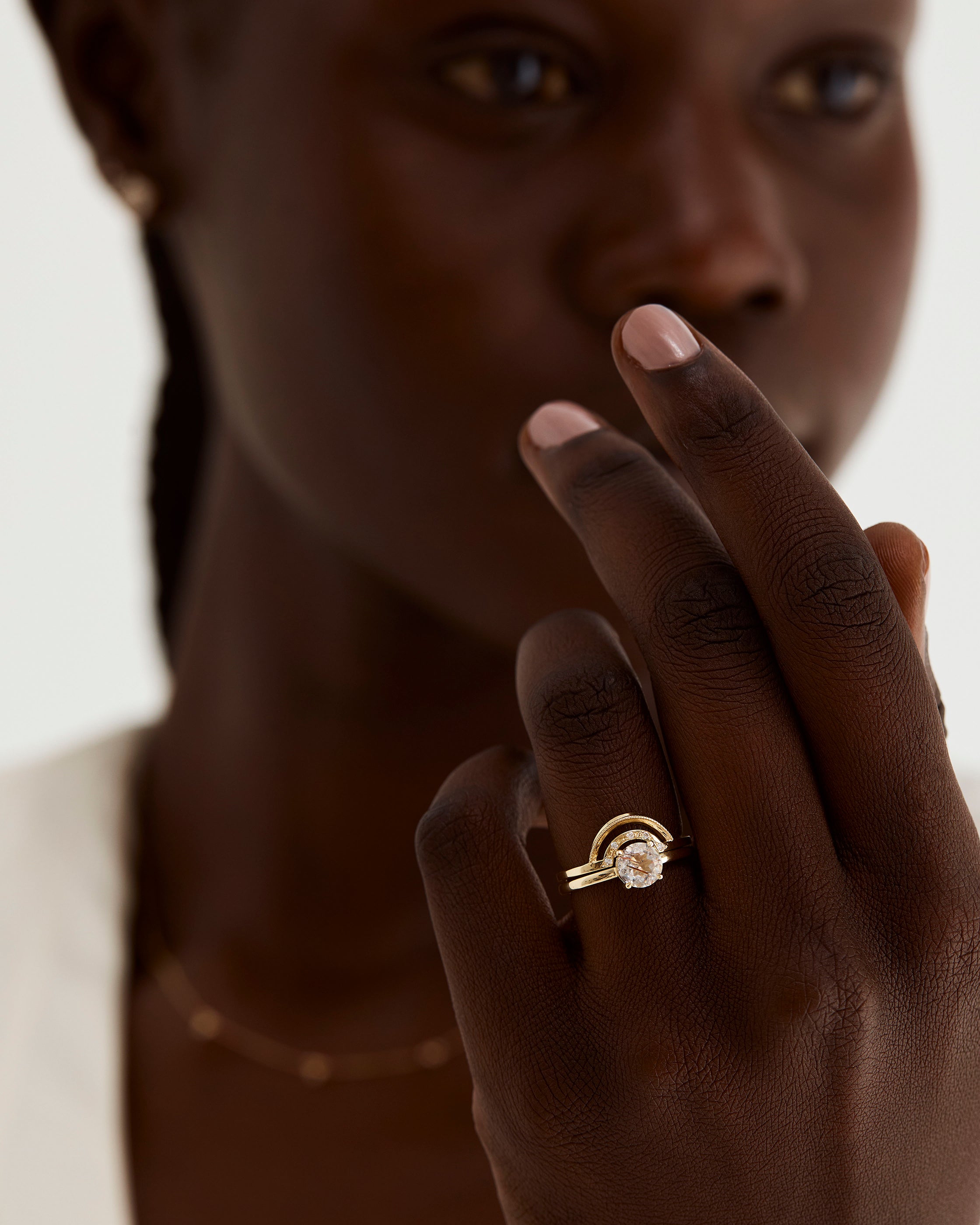 A model wears a double arc crown ring with diamonds stacked with a solitaire style engagement ring.