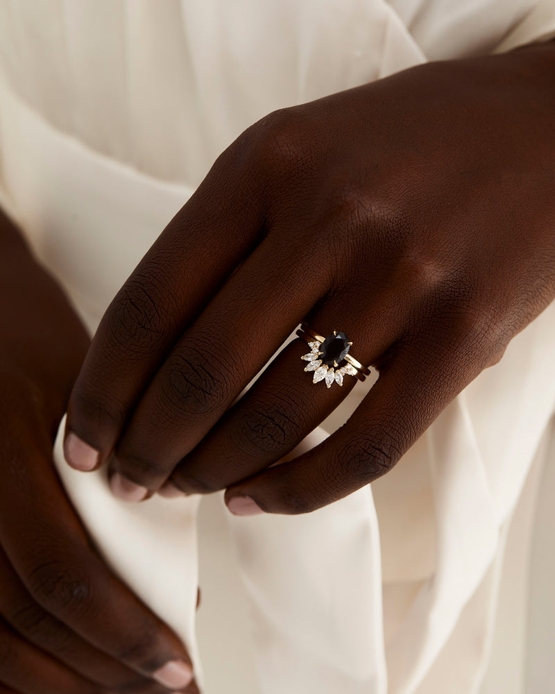 A model wears a diamond sun inspired crown ring stacked with an oval solitaire style engagement ring.