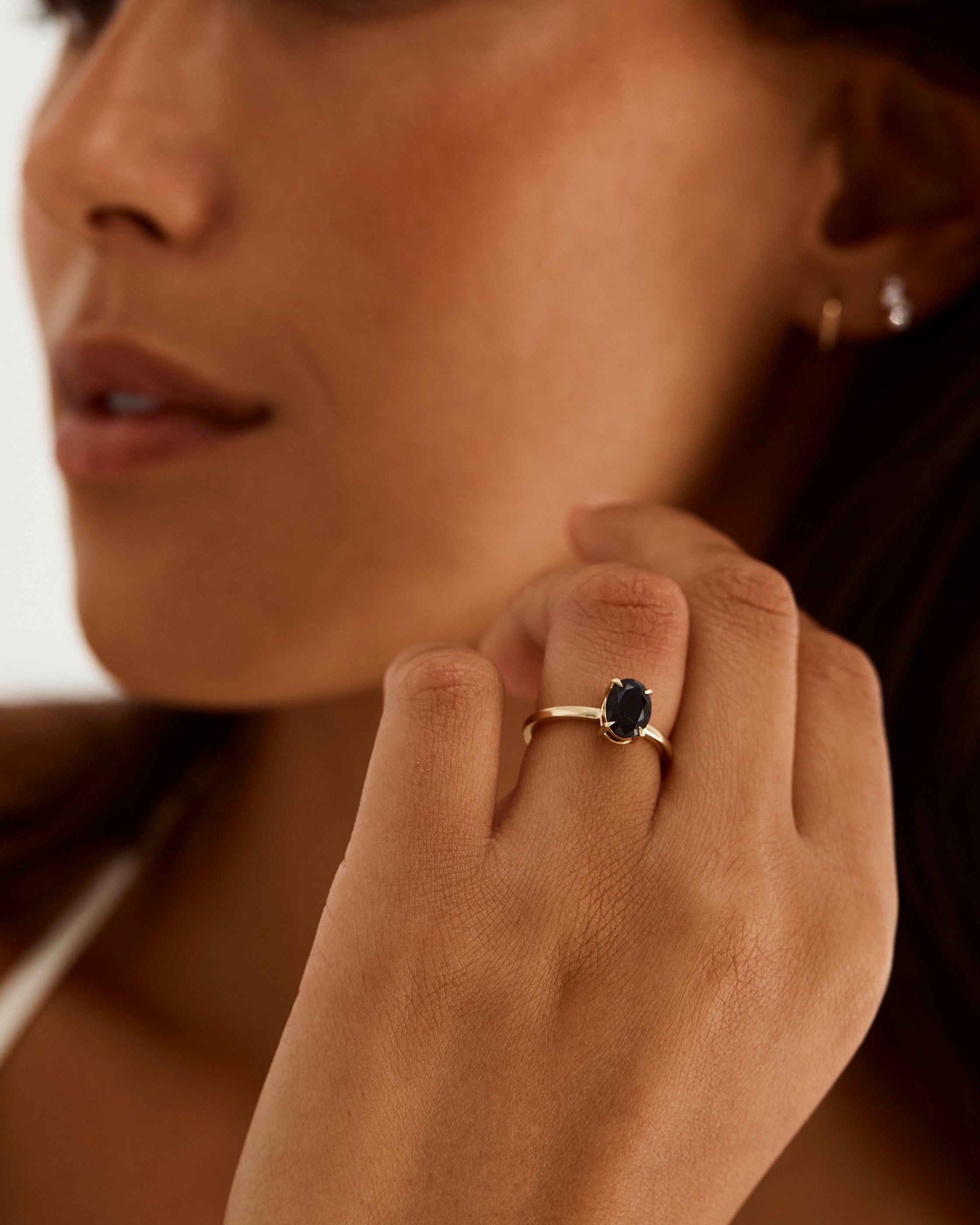 A model wears an oval solitaire style engagement ring with a black spinel.