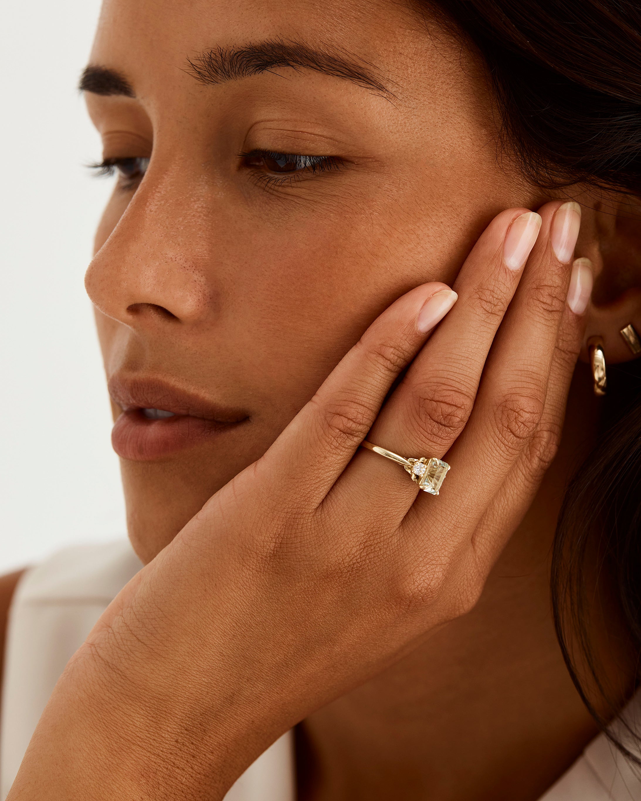 A model wears an emerald cut trio ring featuring petite diamonds and a central green amethyst