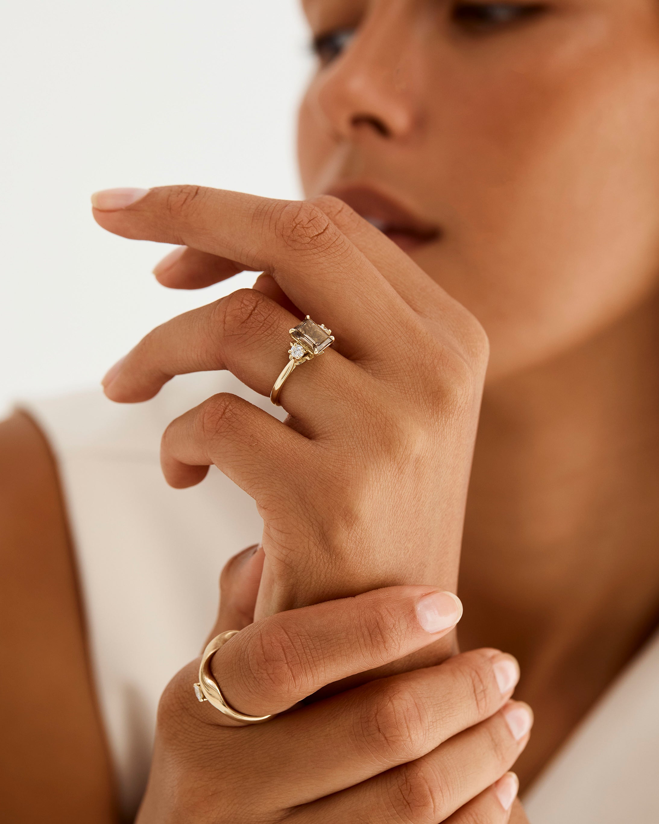 A model wears an emerald cut trio ring featuring petite diamonds and a central smokey quartz