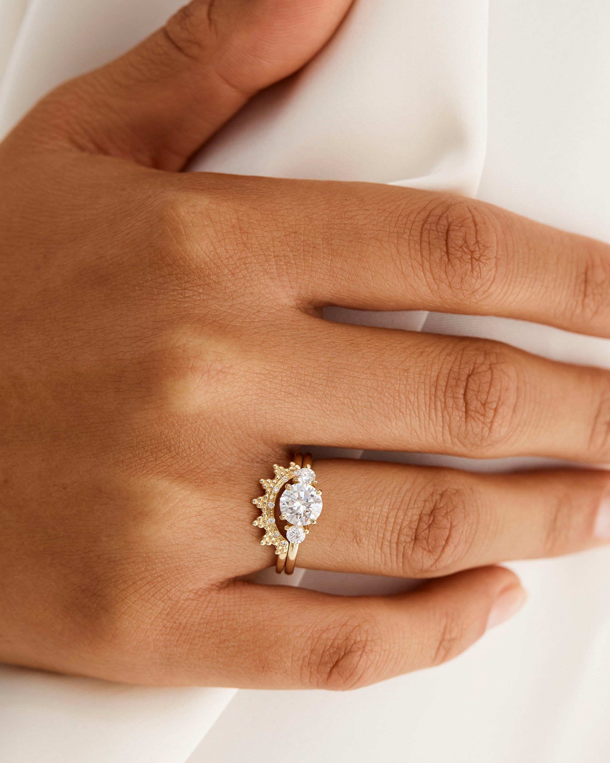 A model wears a diamond dot detailed crown ring stacked with a trio style engagement ring