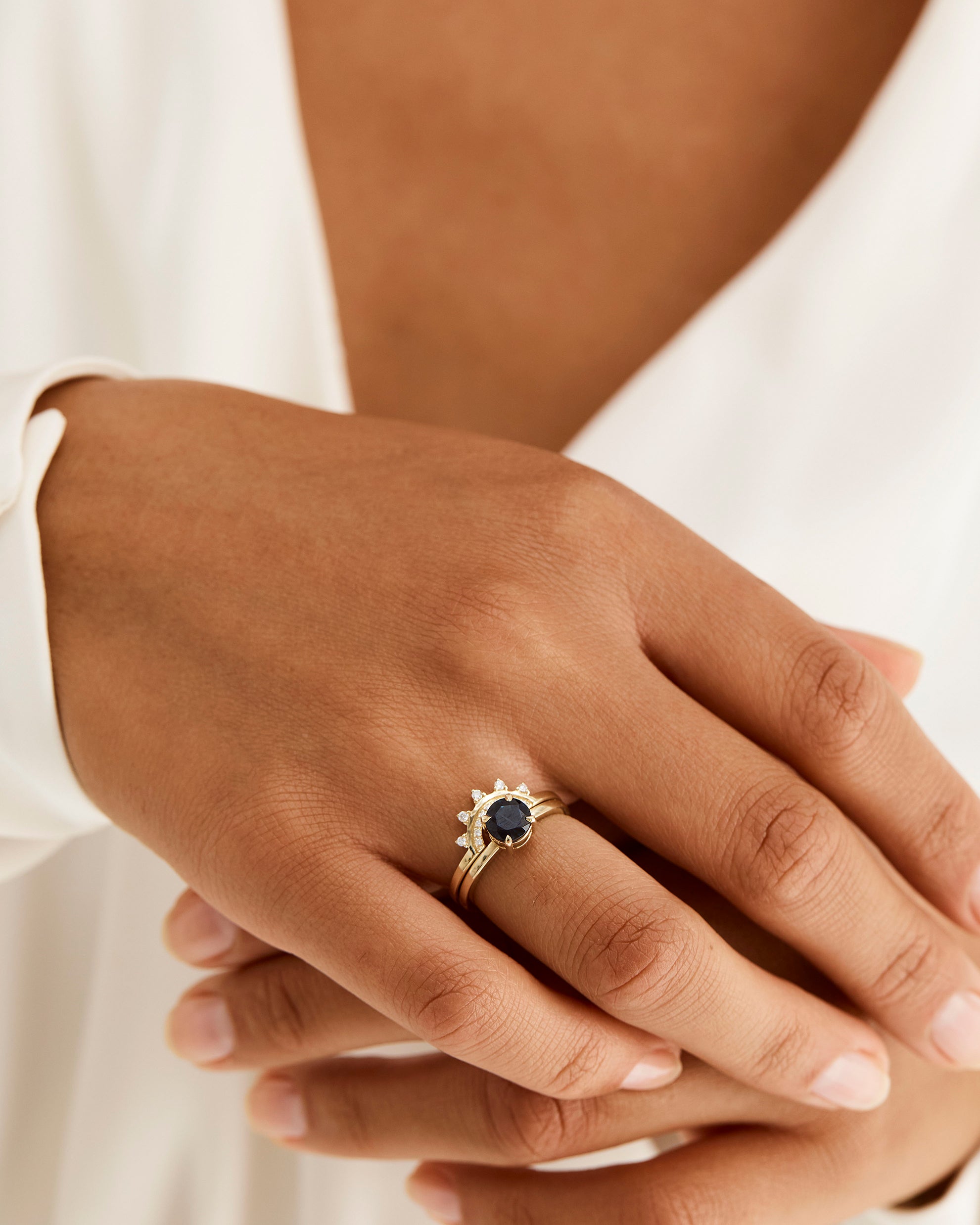 A model wears a detailed diamond crown ring stacked with a solitaire style engagement ring