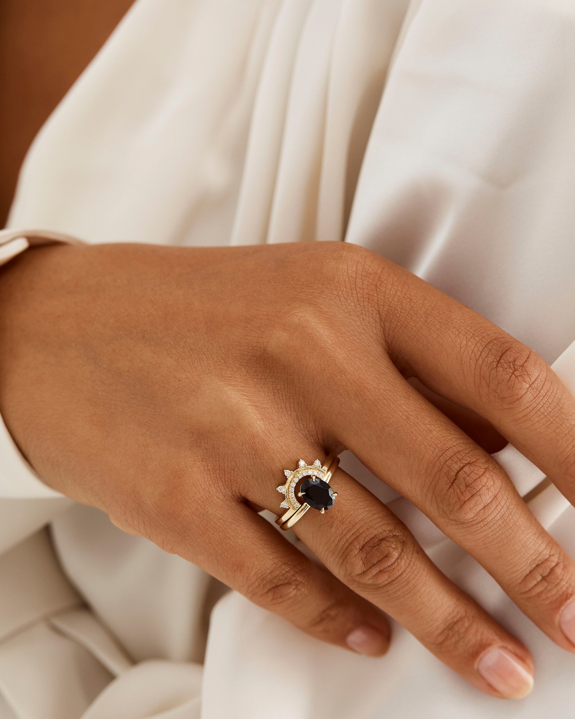 A model wears a detailed diamond crown ring stacked with a solitaire style engagement ring