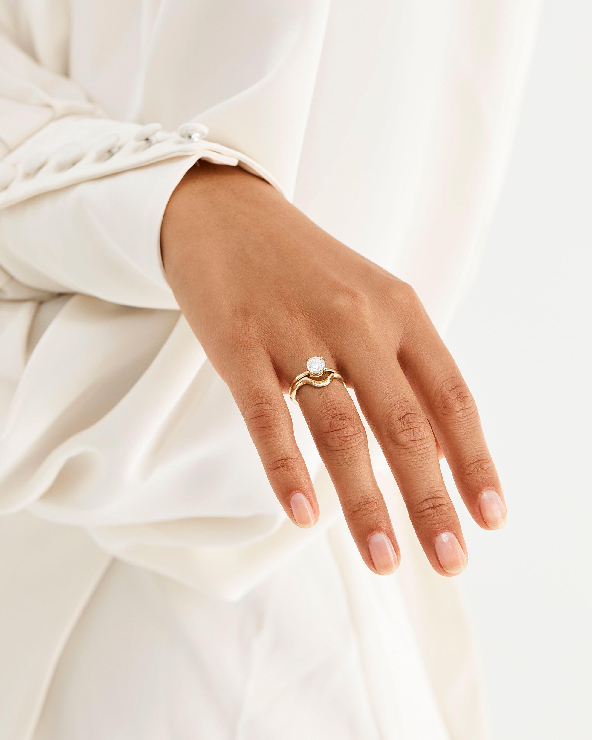 A model wears an organic inspired crown ring stacked with a solitaire style engagement ring
