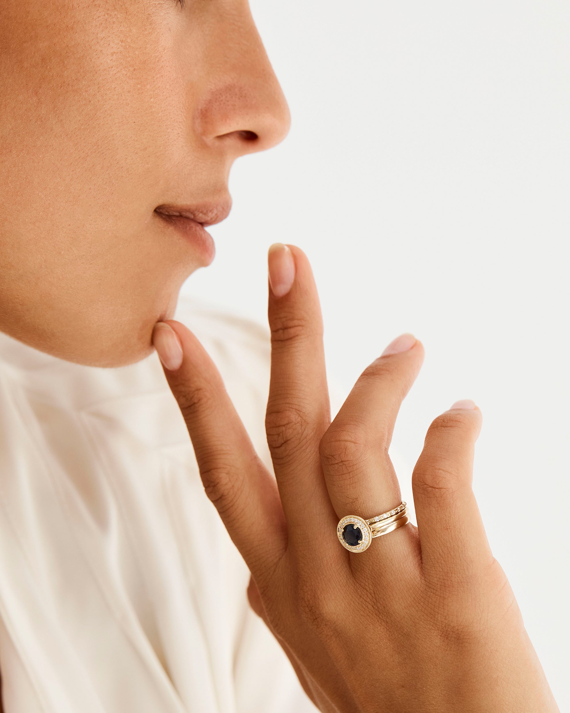 Our cascade white diamond band and classic half round band stacked with a sapphire and diamond round halo engagement ring, worn by a model