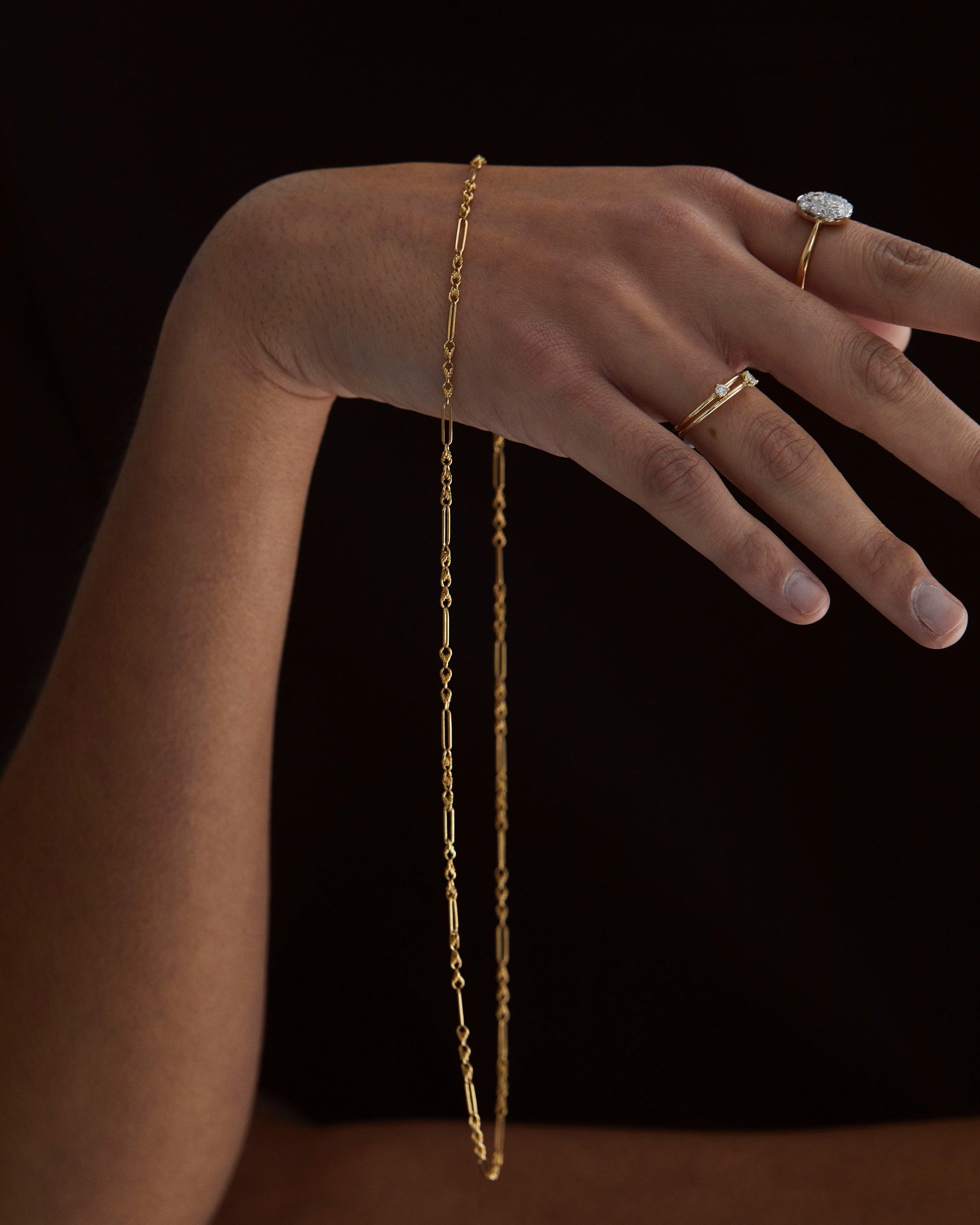 A hand draped with the Helena Vintage Necklace and various NMJ gold rings. 