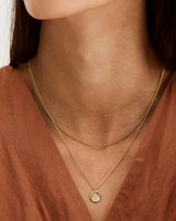 A woman wearing the Nhurali Necklace and the Simple Chain, both in yellow gold.