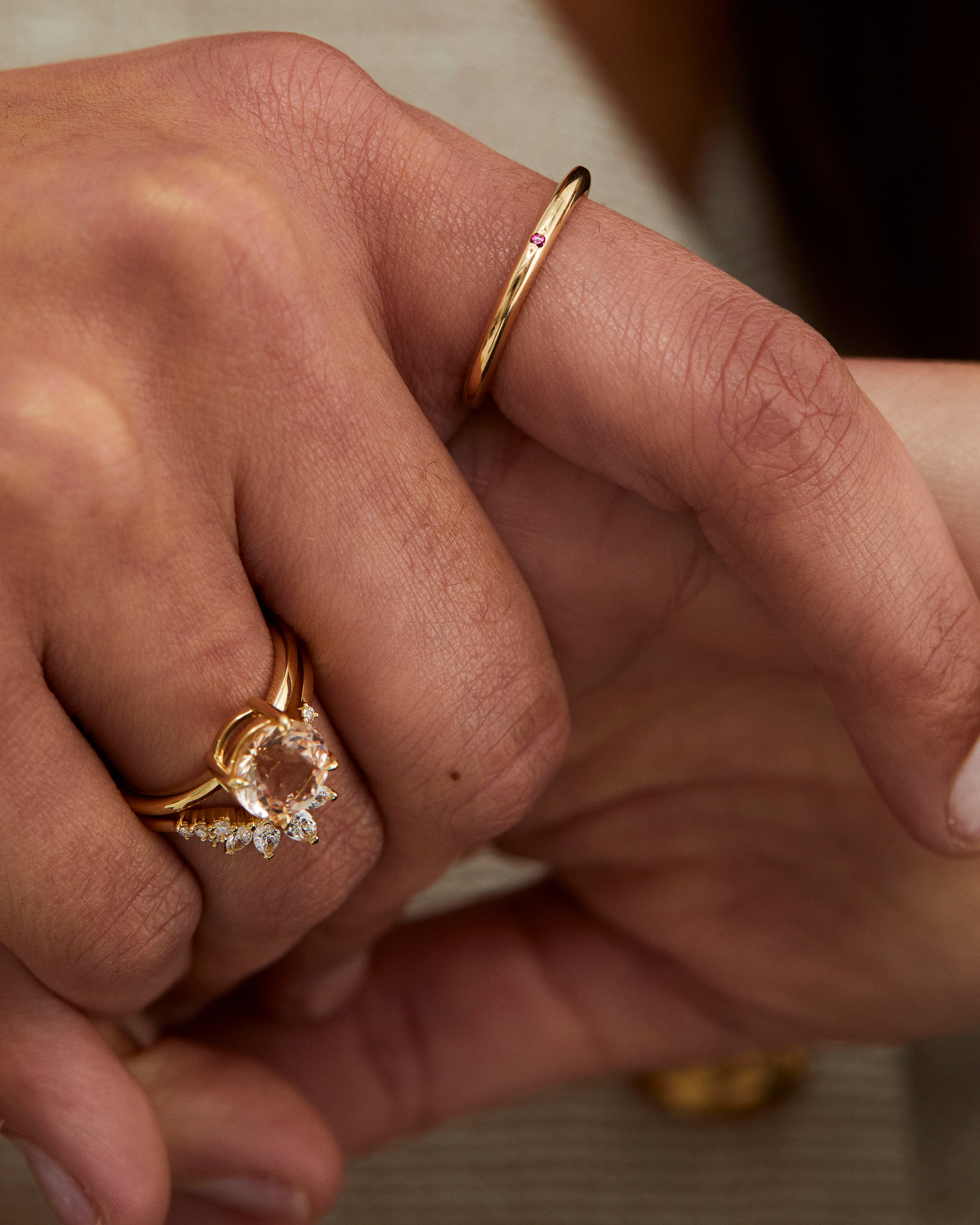 A close up on a hand wearing the Promise Ring with a ruby, alongside ceremonial pieces in yellow gold.