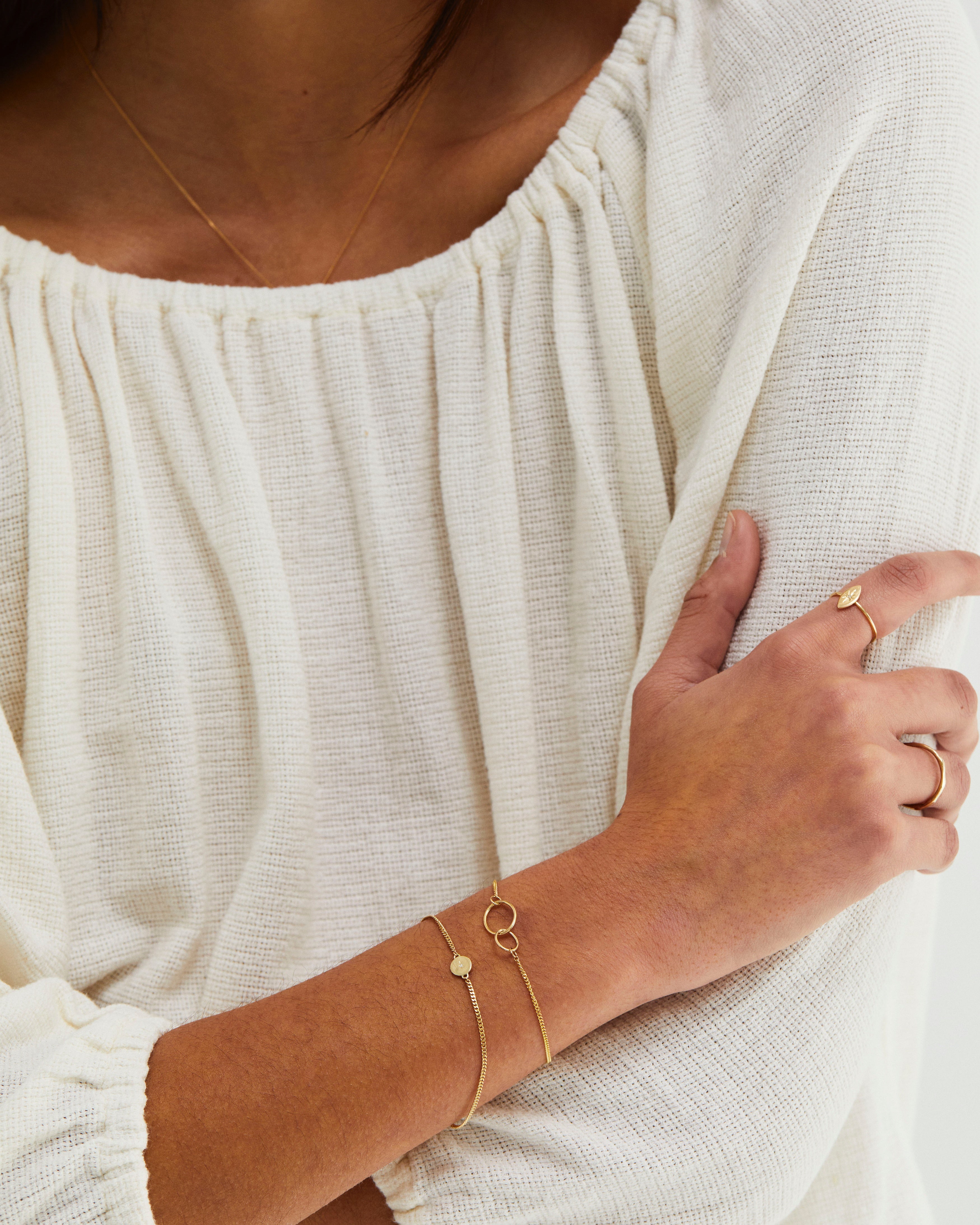 A woman wearing the Loop Through Oval Bracelet paired with the Eily Bracelet | Birthstone, both in yellow gold.