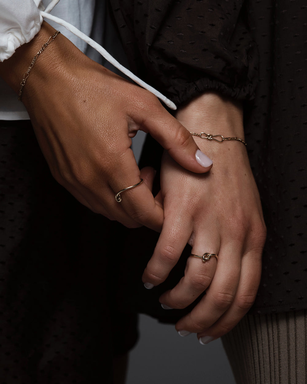 Two hands held, adorned with the Cara Ring and the Anam Charm Bracelets