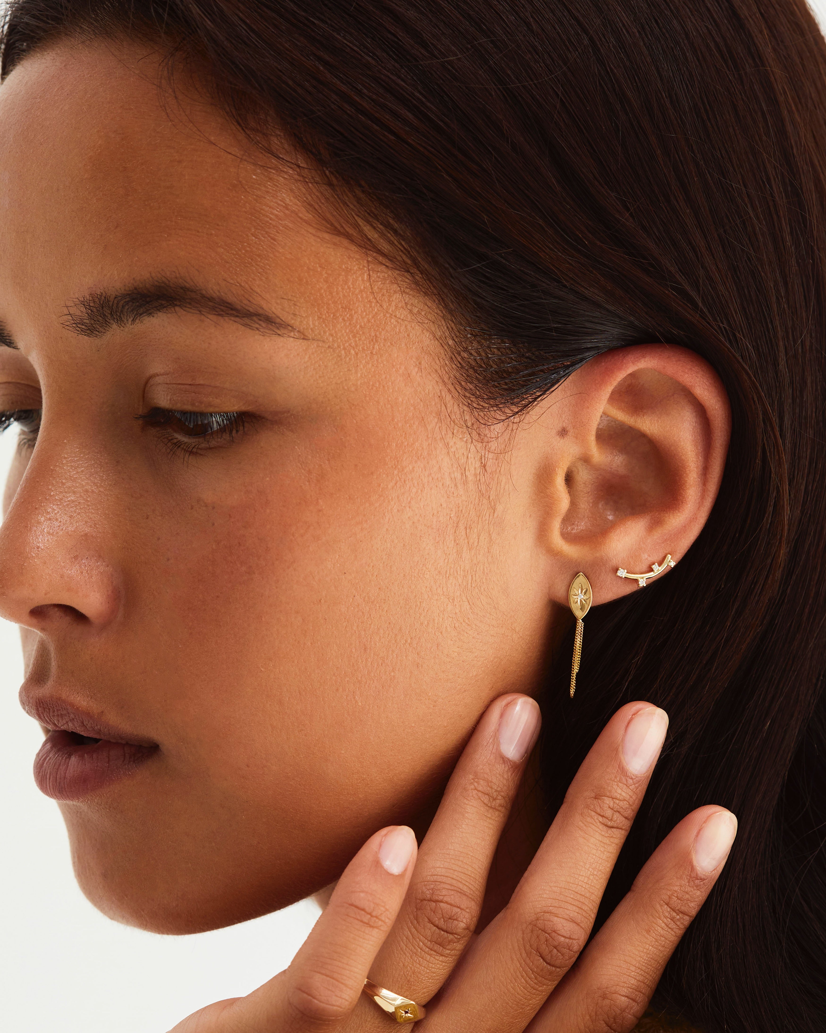 Womean wearing gold earring with a white diamond and a loop chain