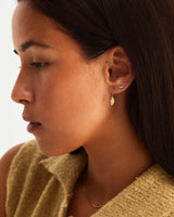 Woman wearing gold arced shaped earrings set with white diamonds