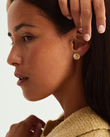 A woman wearing the Pan Earrings, paired with the Tiny Dot Stud, both in yellow gold.