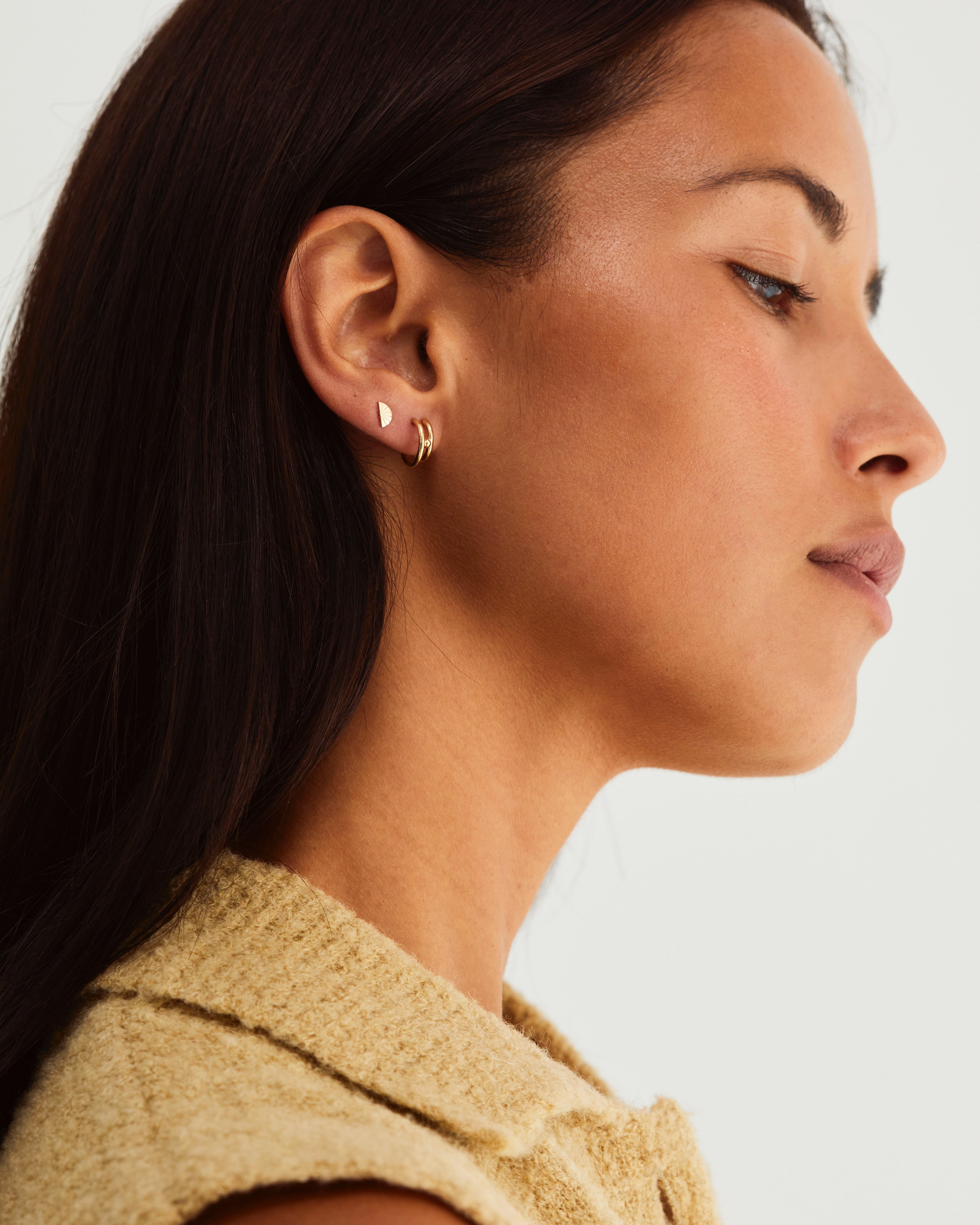A model wearing the Double Reliquum Hoops and the Jia Studs, both in yellow gold.