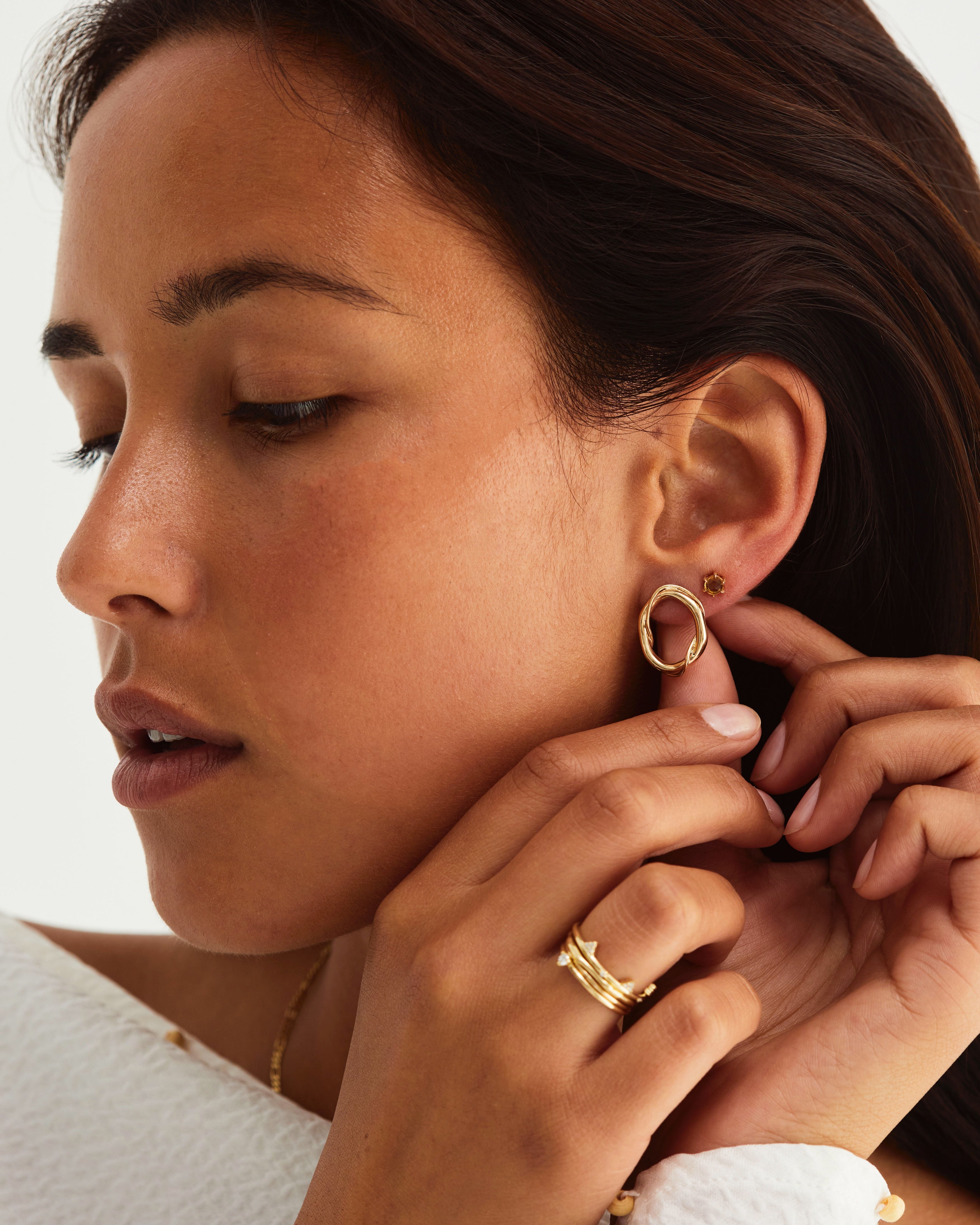 Woman wearing gold hoops and small studs featuring a honey quartz coloured stone