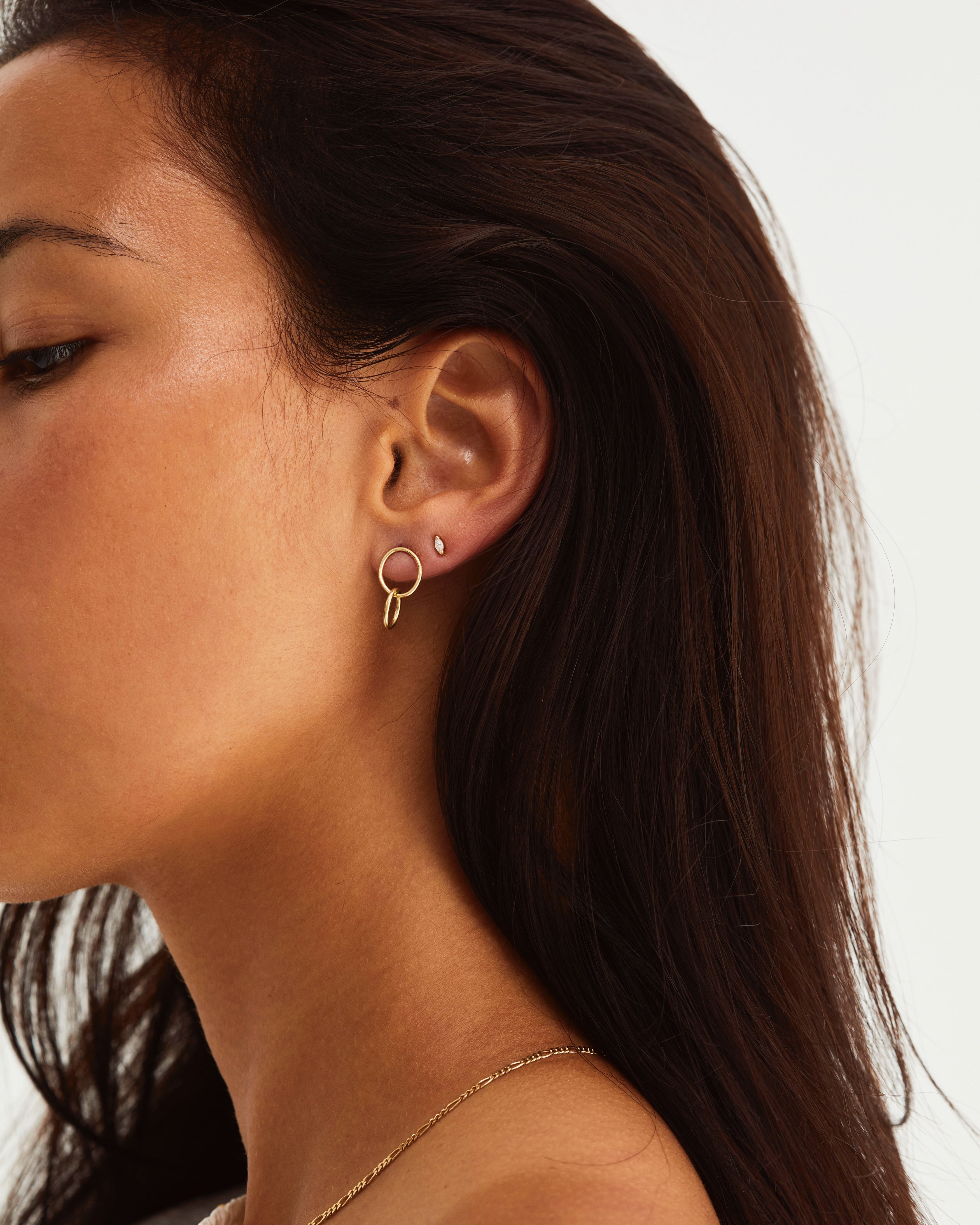 A woman wearing the Loop Through Oval Studs and the Vega Studs | Diamond, both in yellow gold.