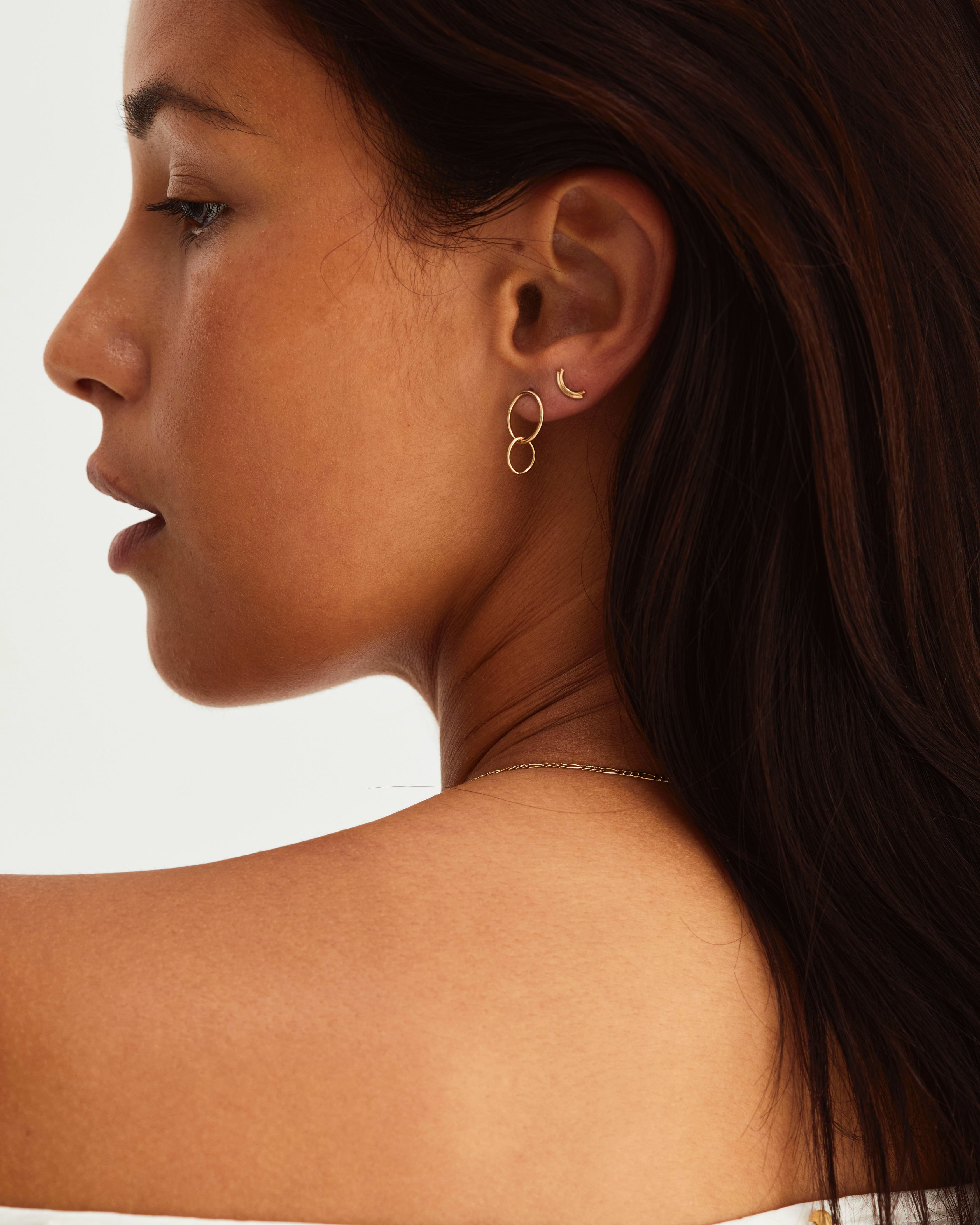 A woman wearing the Loop Through Oval Studs and the Lai Studs in yellow gold.