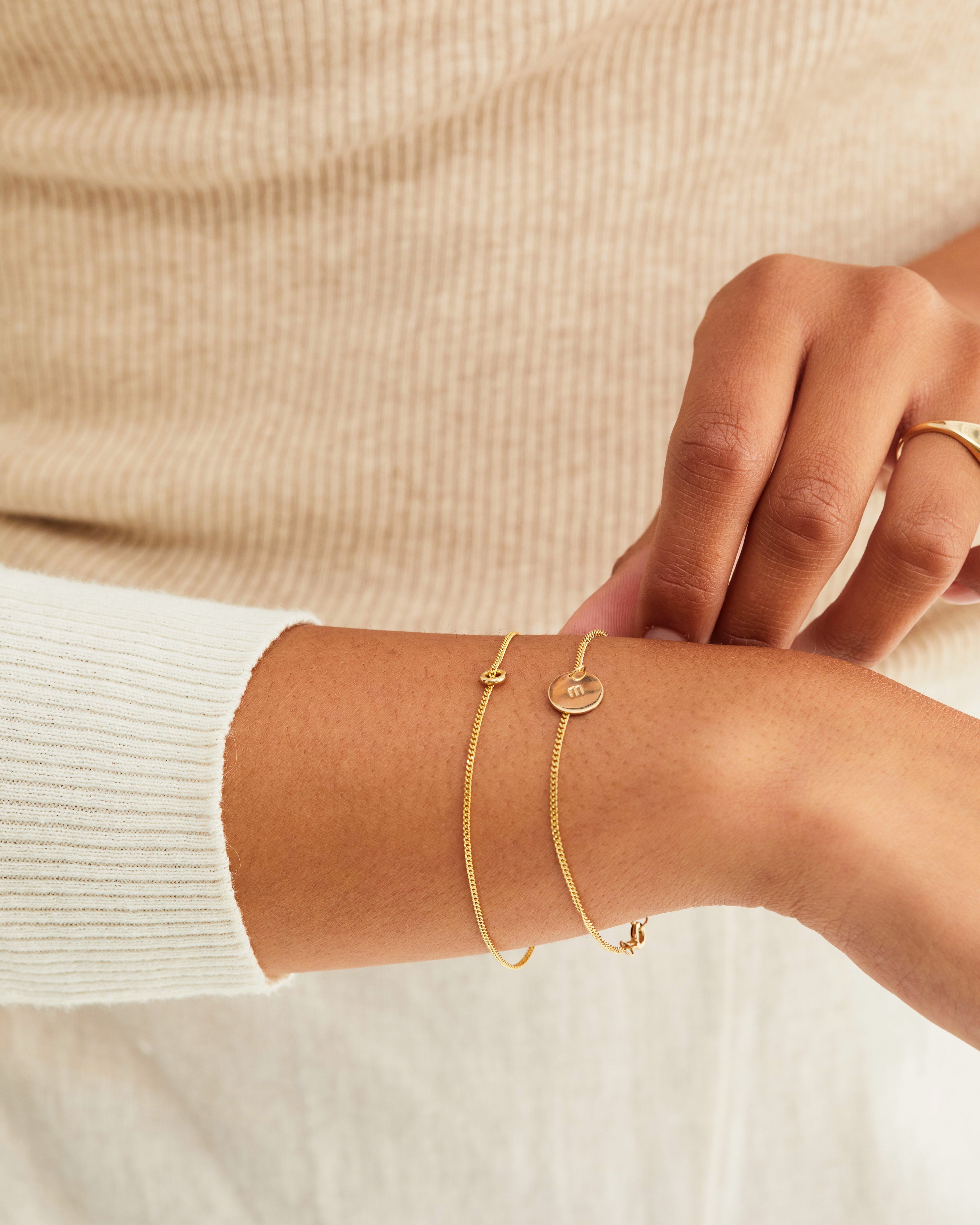 A woman wearing the Aether Charm Bracelet | Birthstone and the Mini Initial Bracelet, both in yellow gold.