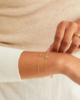 A woman wearing the Aether Charm Bracelet | Birthstone and the Mini Initial Bracelet, both in yellow gold.