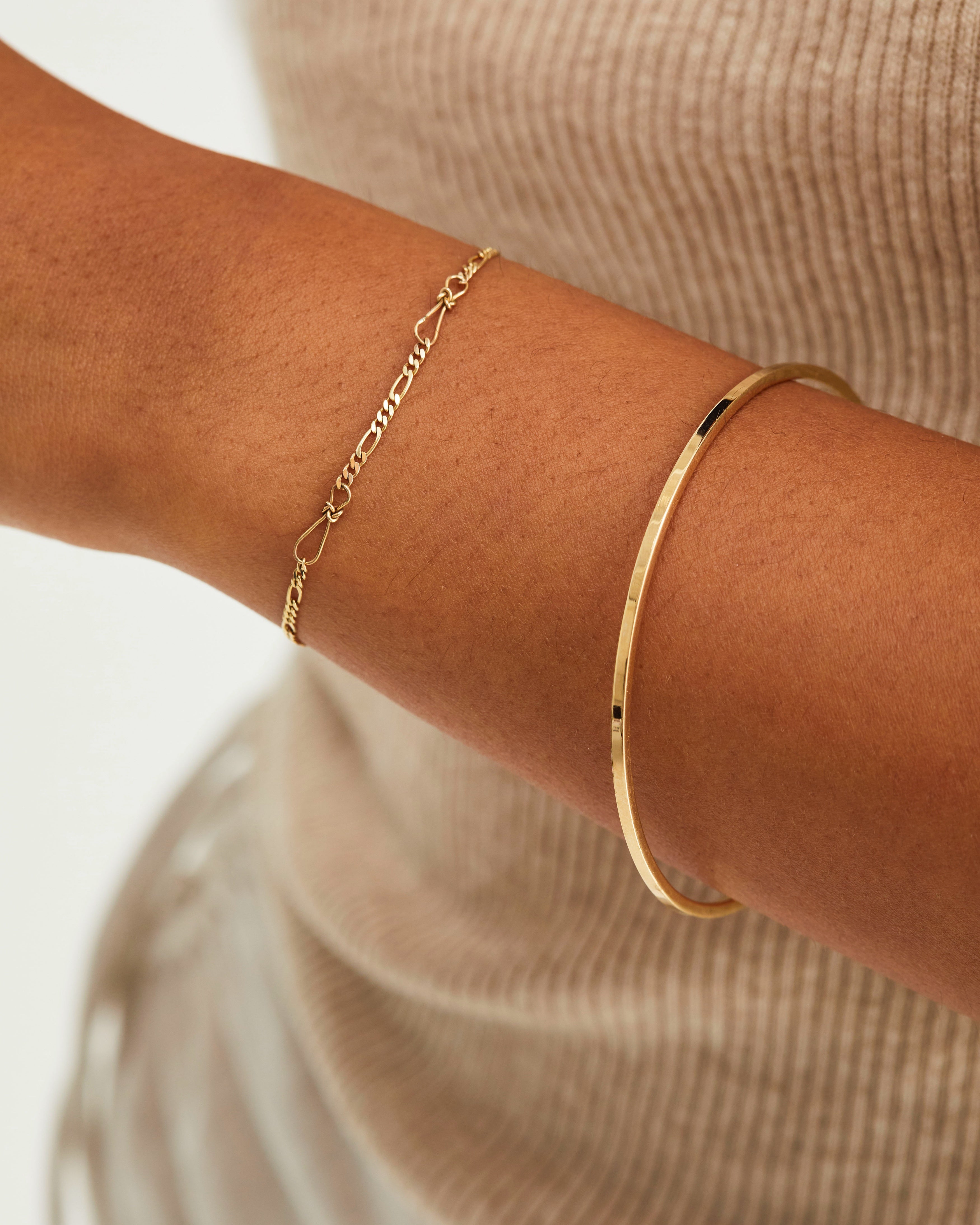 A woman wearing the Anam Charm Bracelet and the Antares Bangle, both in yellow gold.